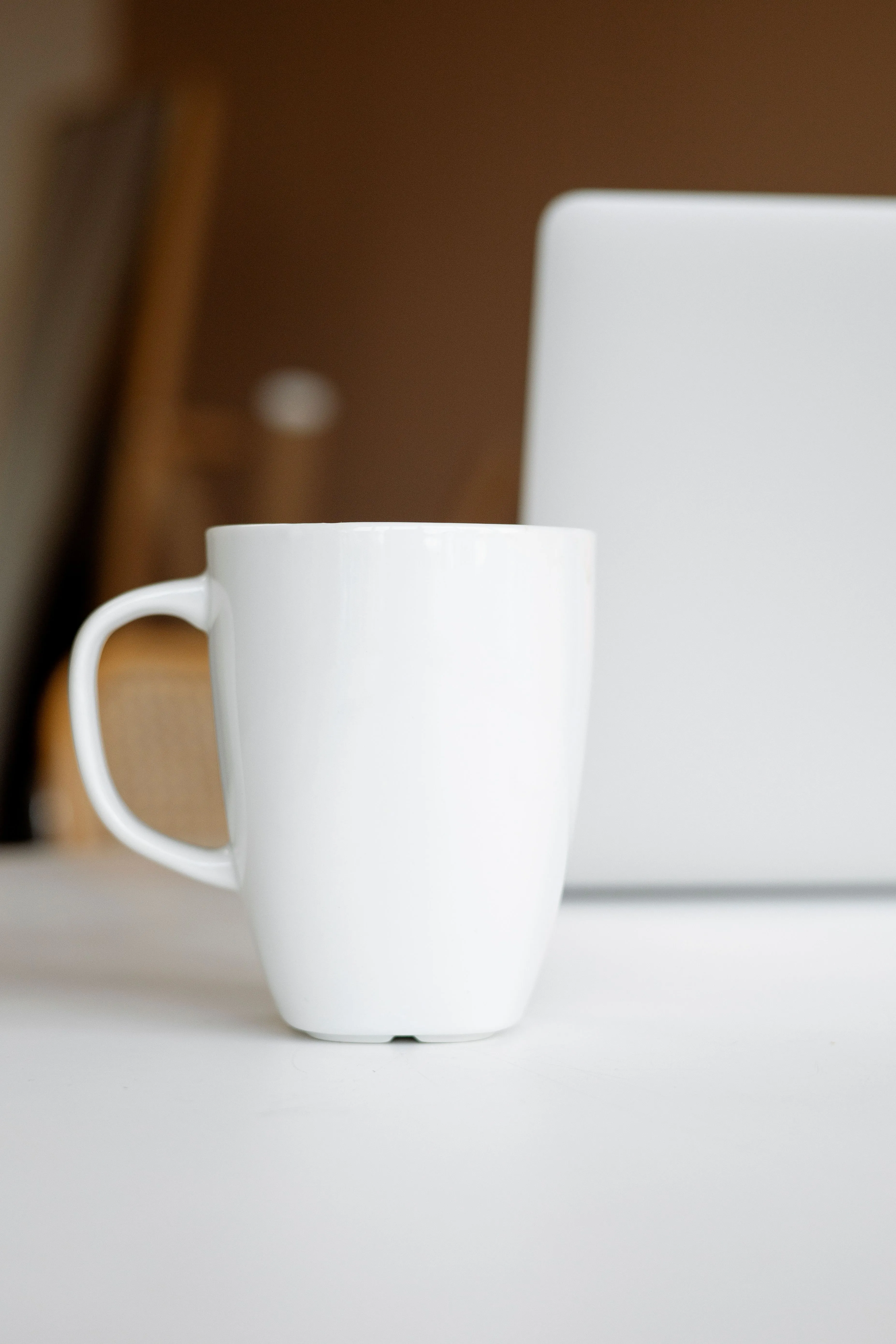 Simple white ceramic mug on desk near laptop, modern minimalism.