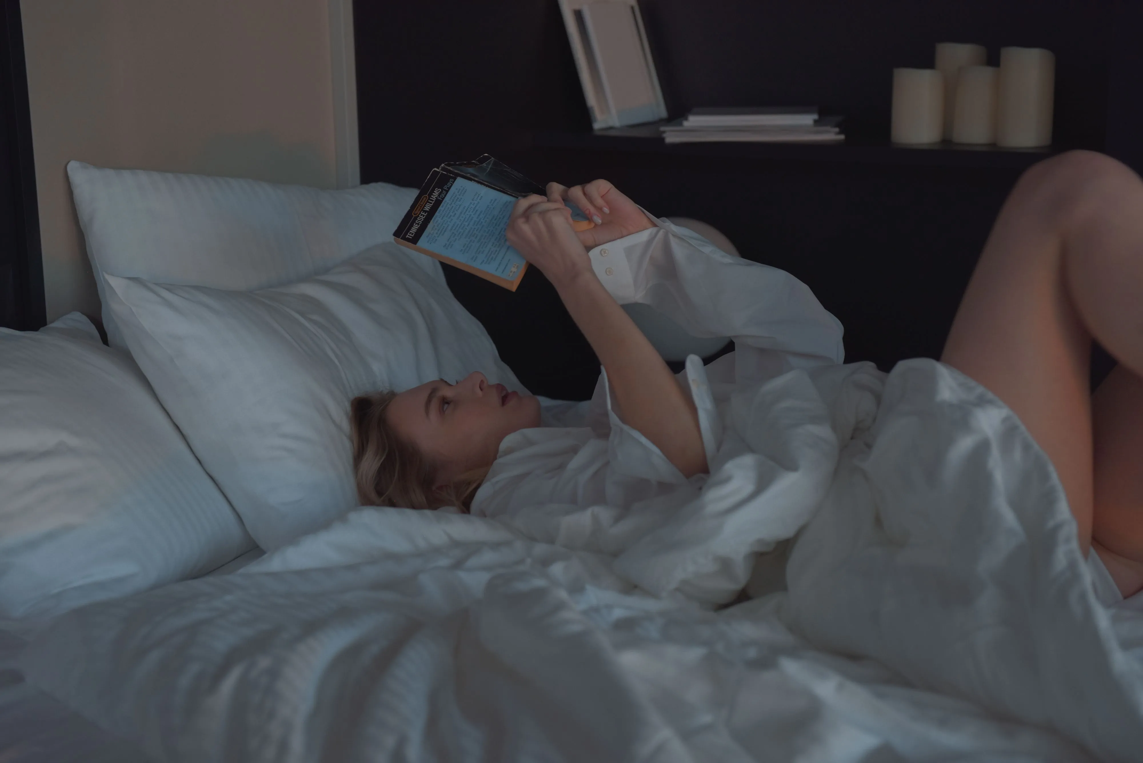 A woman comfortably reading a book in a cozy bedroom setting.