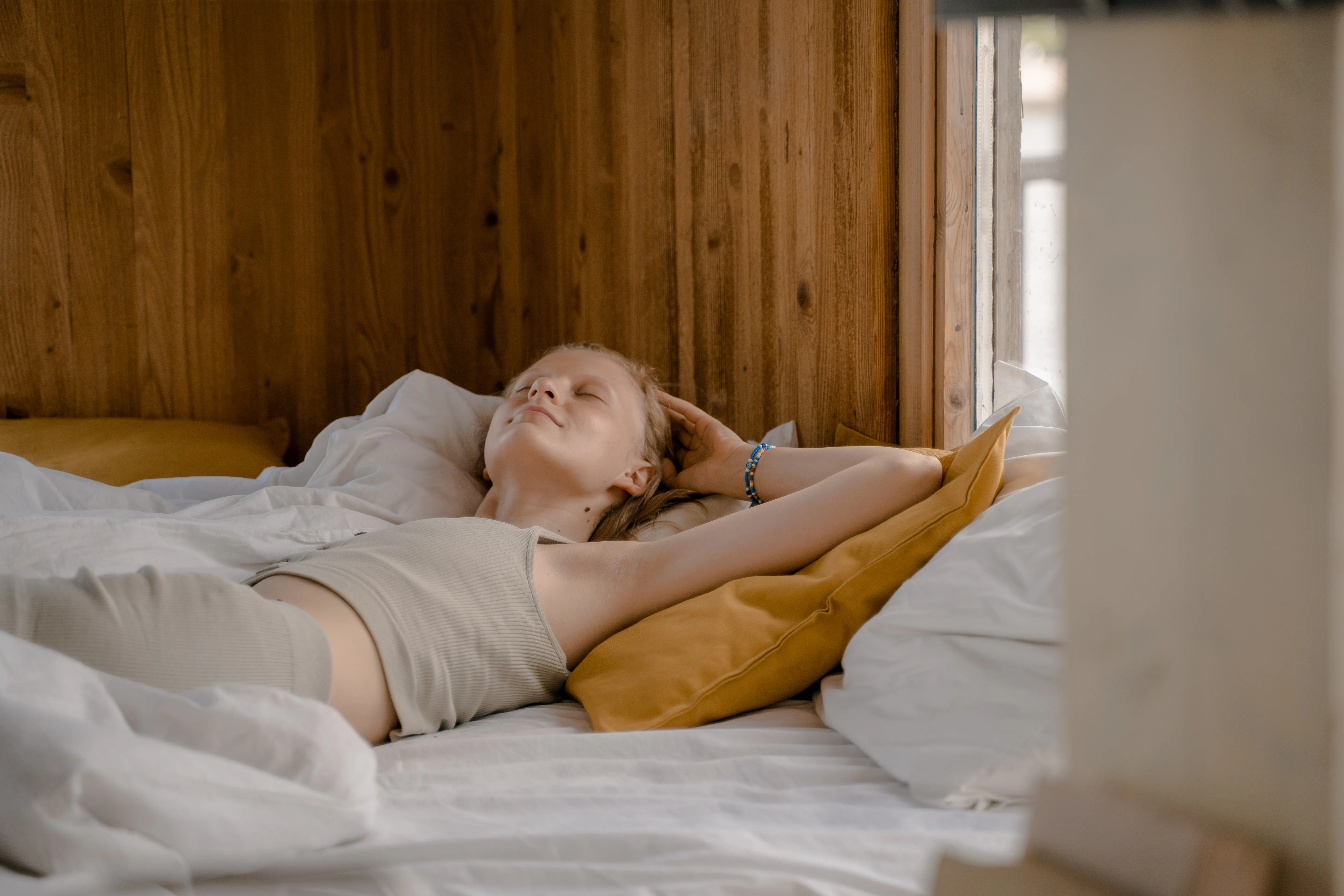 A woman enjoys a tranquil moment lying on her back in a cozy wooden bedroom.