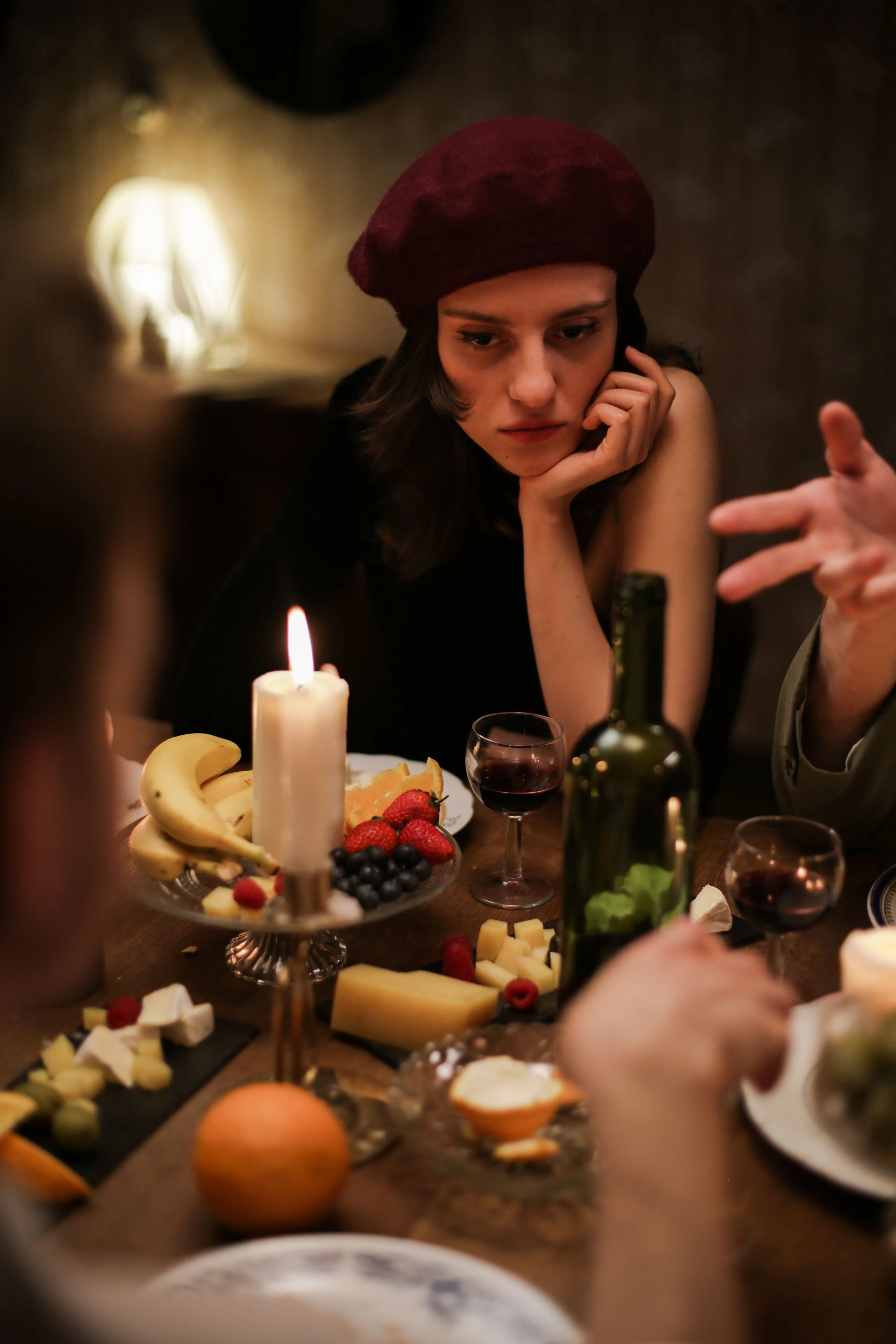 A cozy candlelit dinner featuring a French beret-wearing woman surrounded by food and wine.