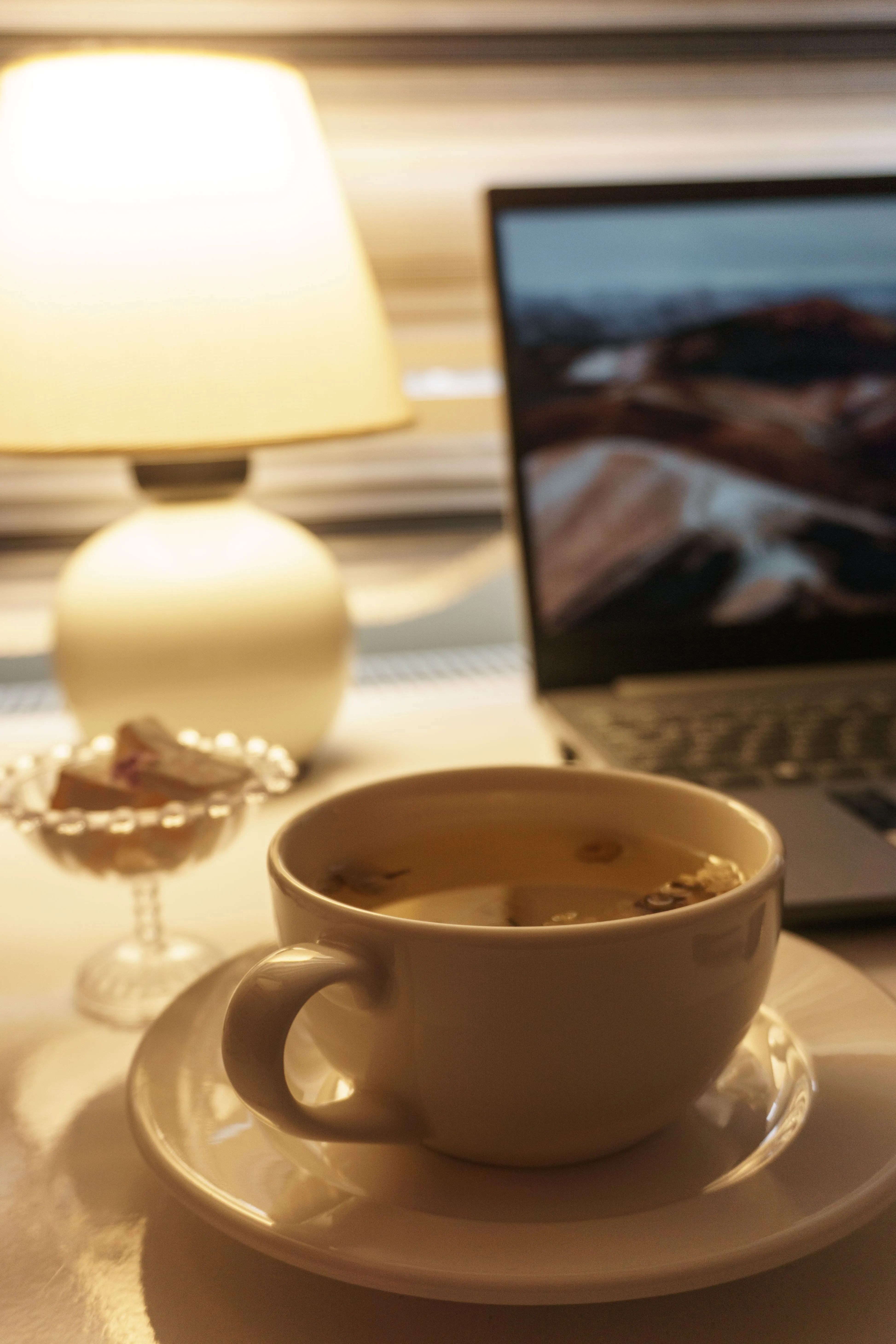 Warm indoor scene with a cup of tea, open laptop, and ambient lamp lighting.