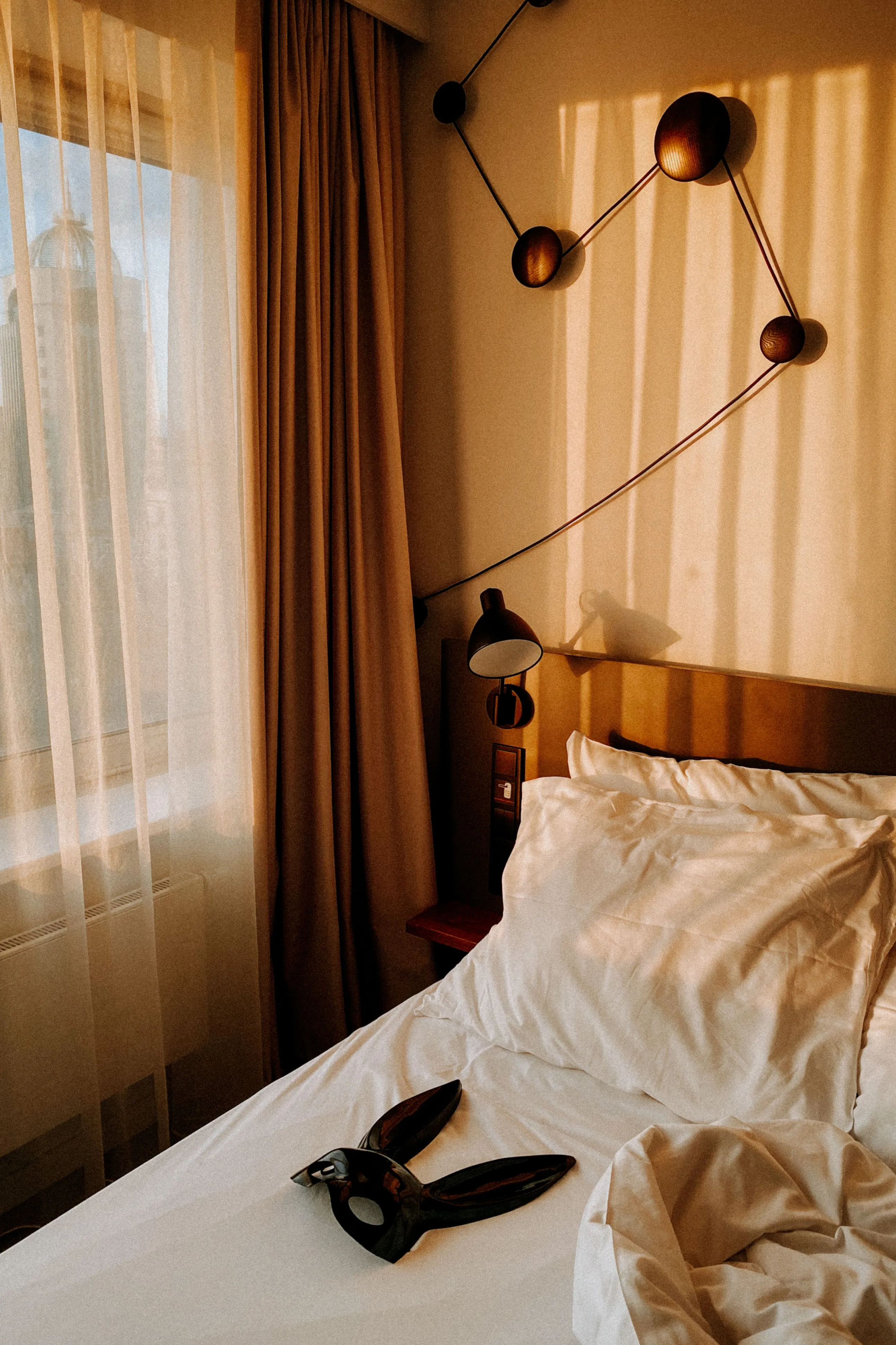 Warm sunlight fills a cozy bedroom with a bedside lamp and wall art above a comfortable bed.