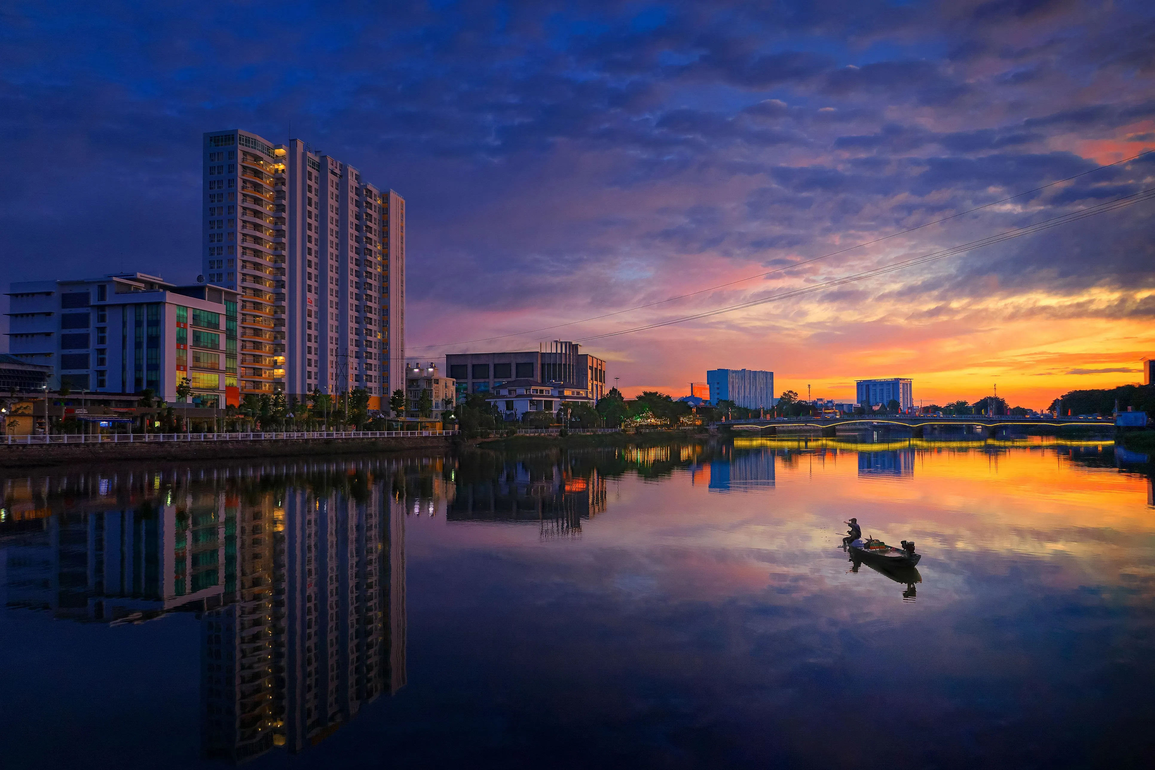 Peaceful cityscape of Long Xuyên at dawn with a calm river reflection.