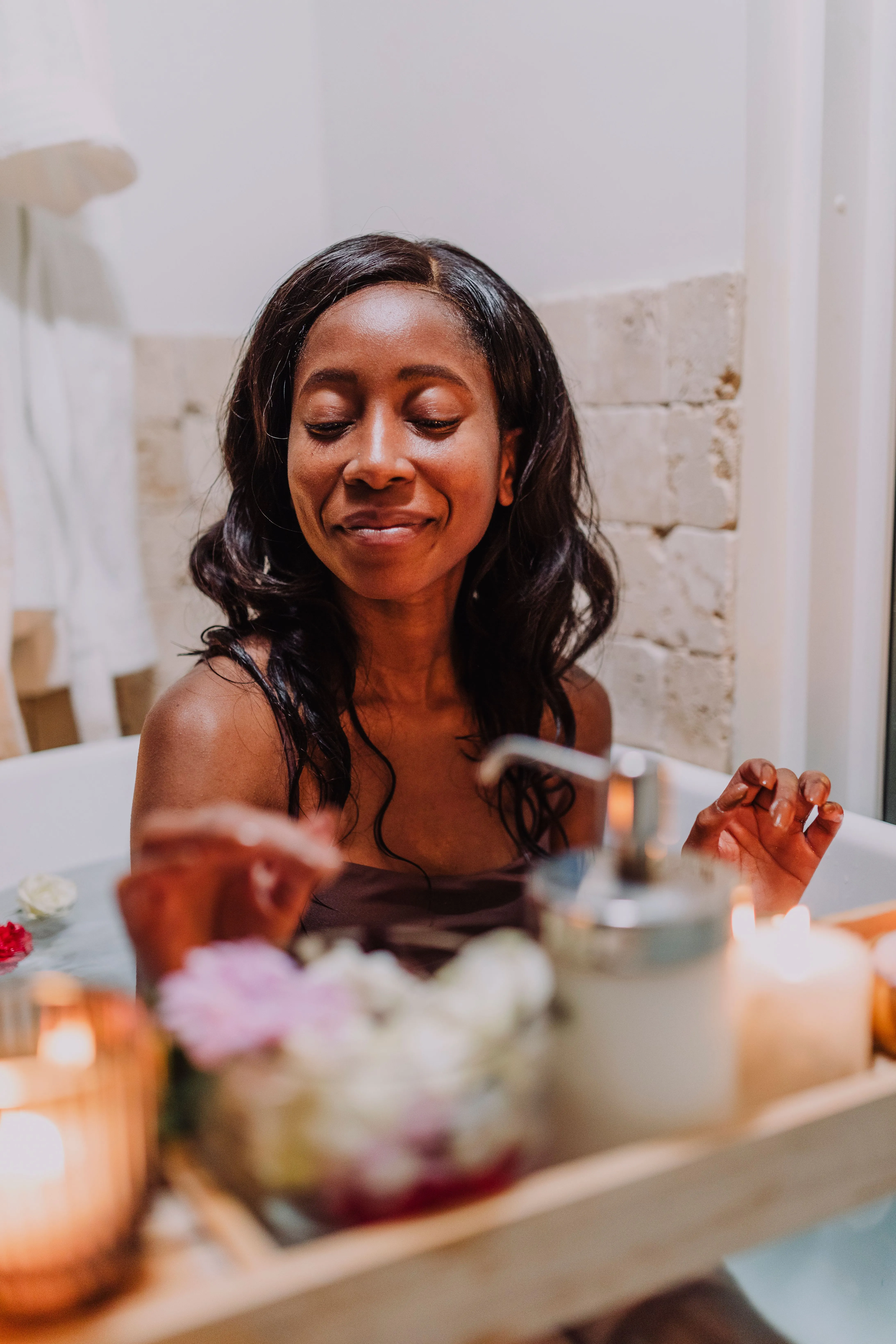 A woman enjoys a calming bath surrounded by flowers and candles for a soothing experience.