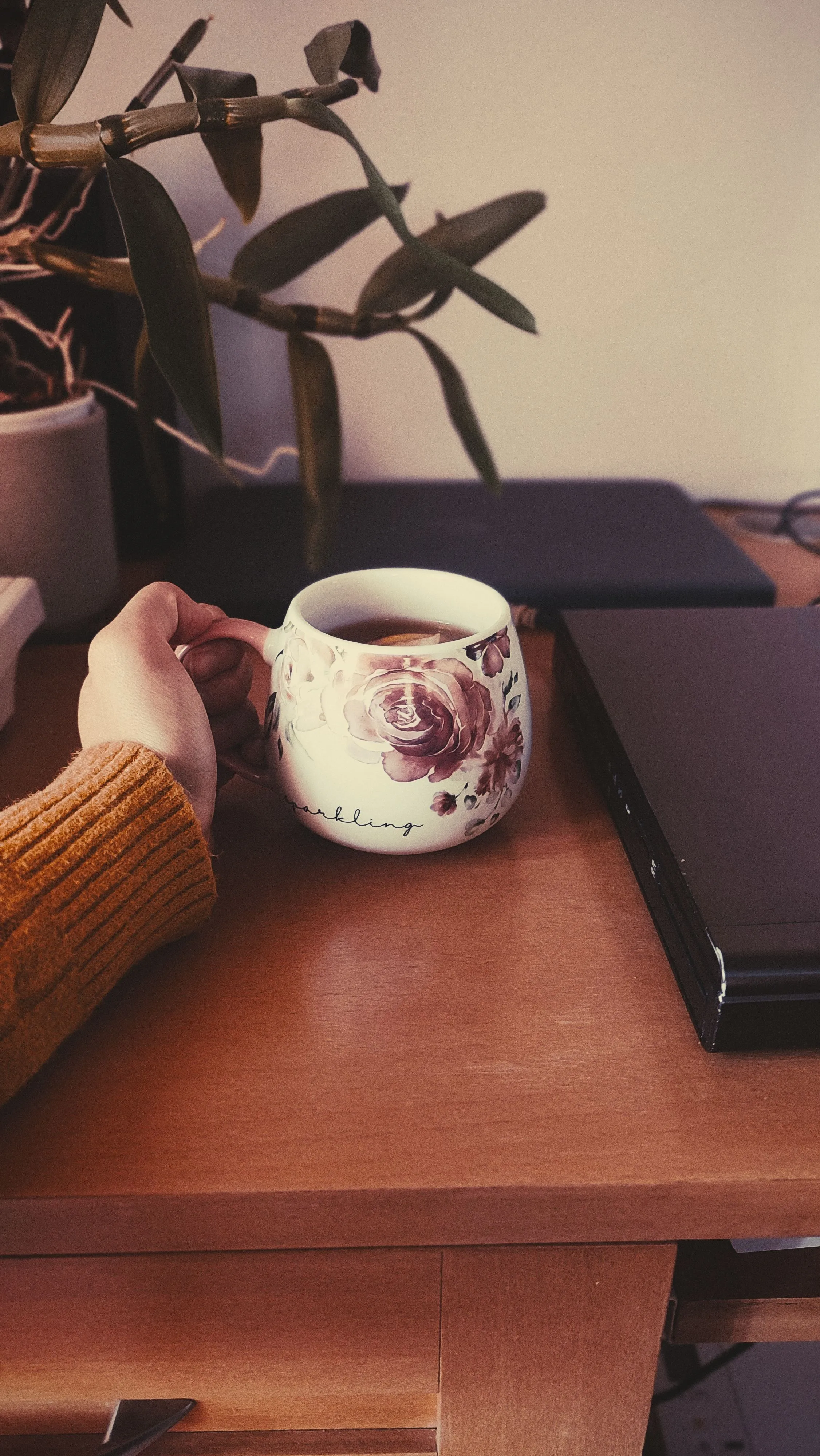 A comforting cup of tea held near a laptop in a cozy home office scene.