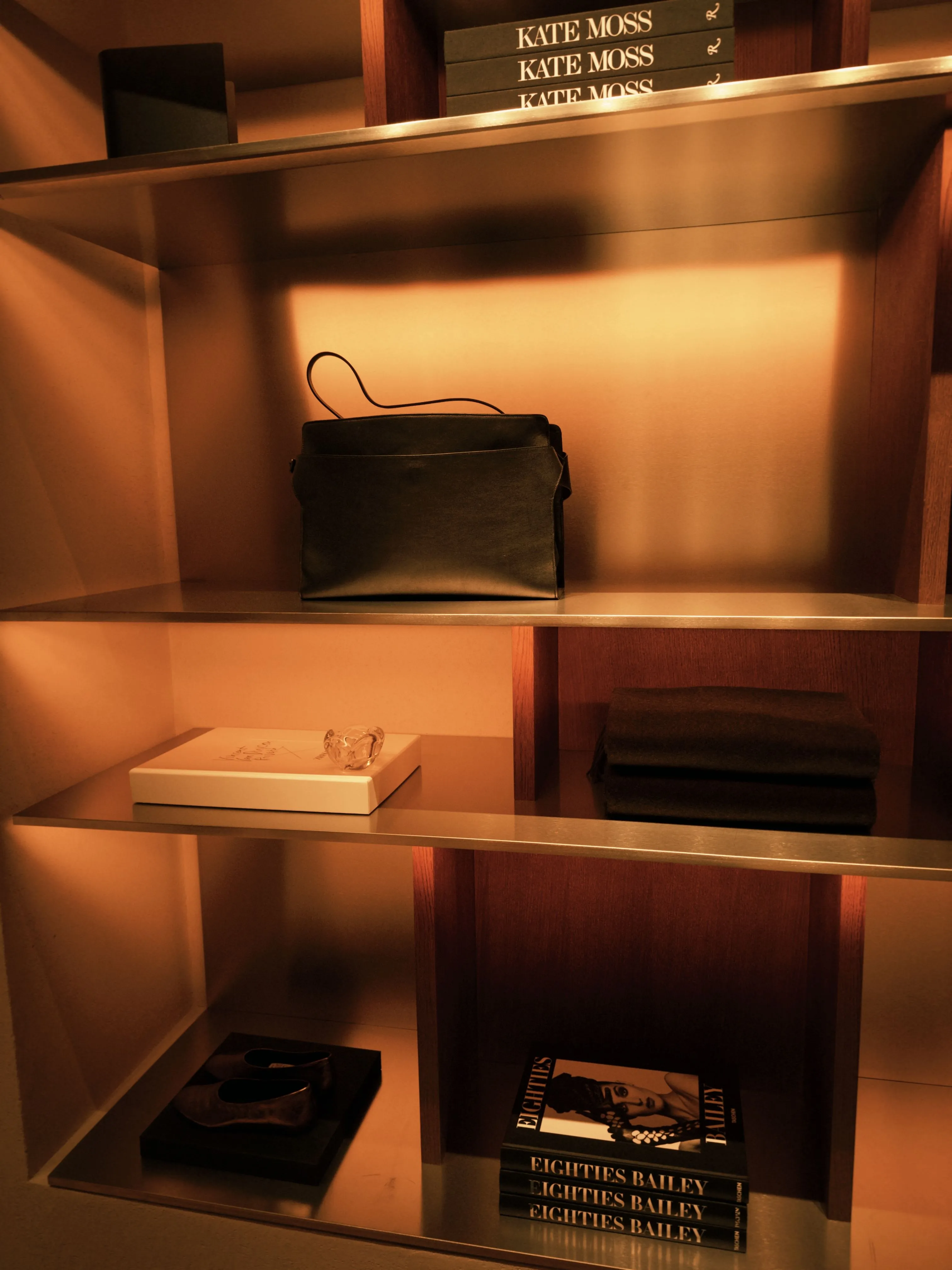 Stylish shelf featuring books, bag, and decor items with warm lighting.