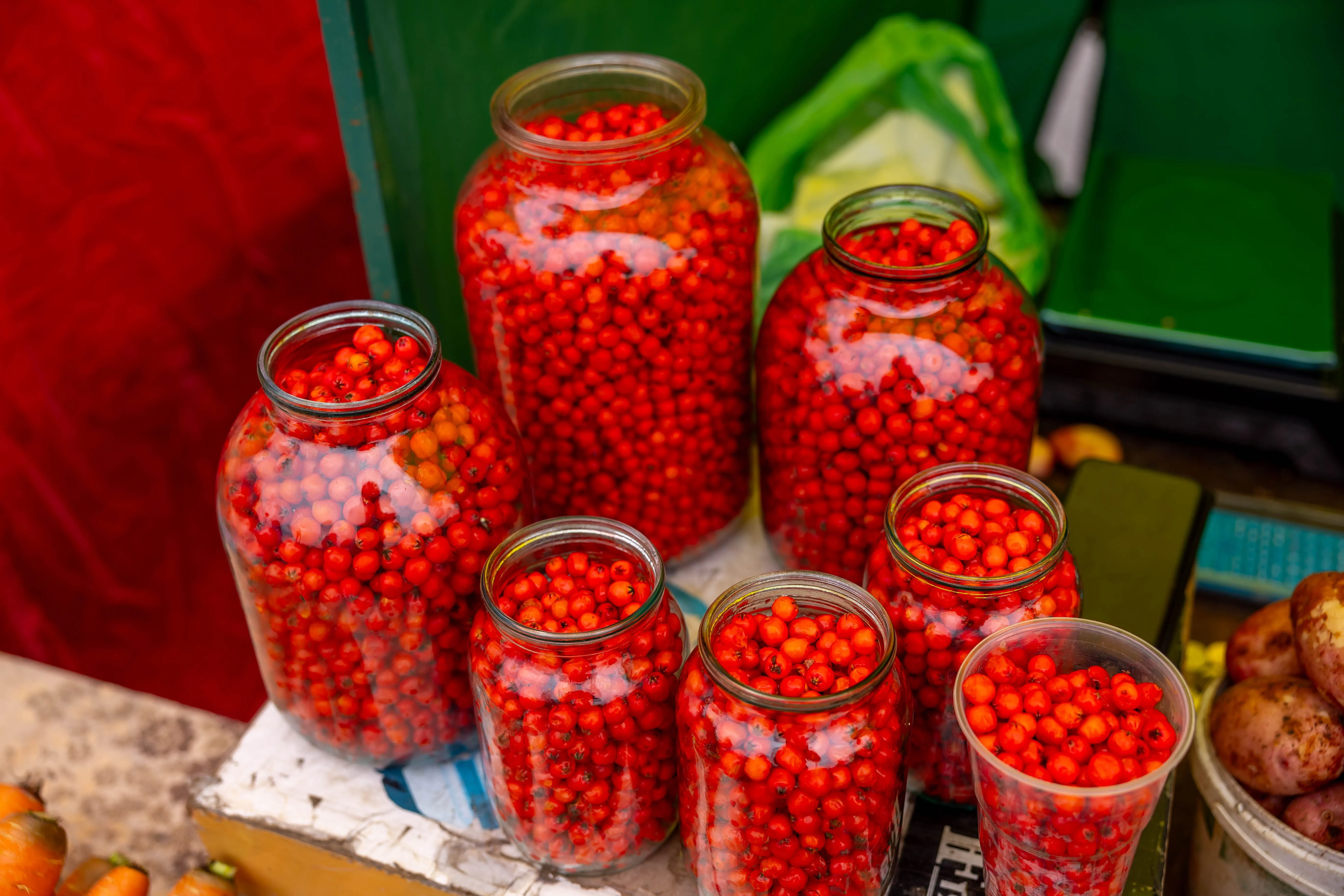 Colorful assortment of bright red berries stored in glass jars on a market stall table.