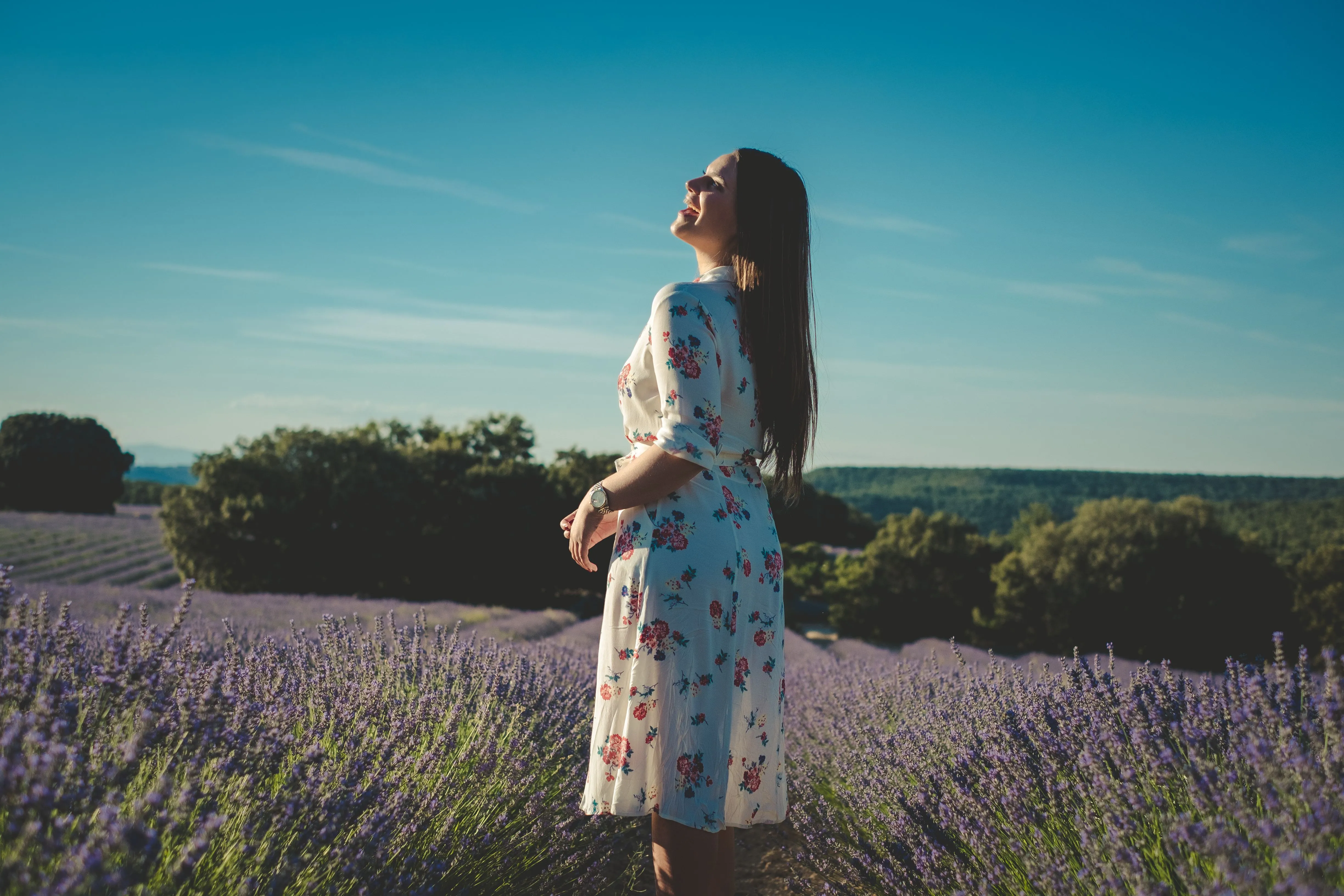 A woman in a floral dress enjoys the lavender field on a sunny day.