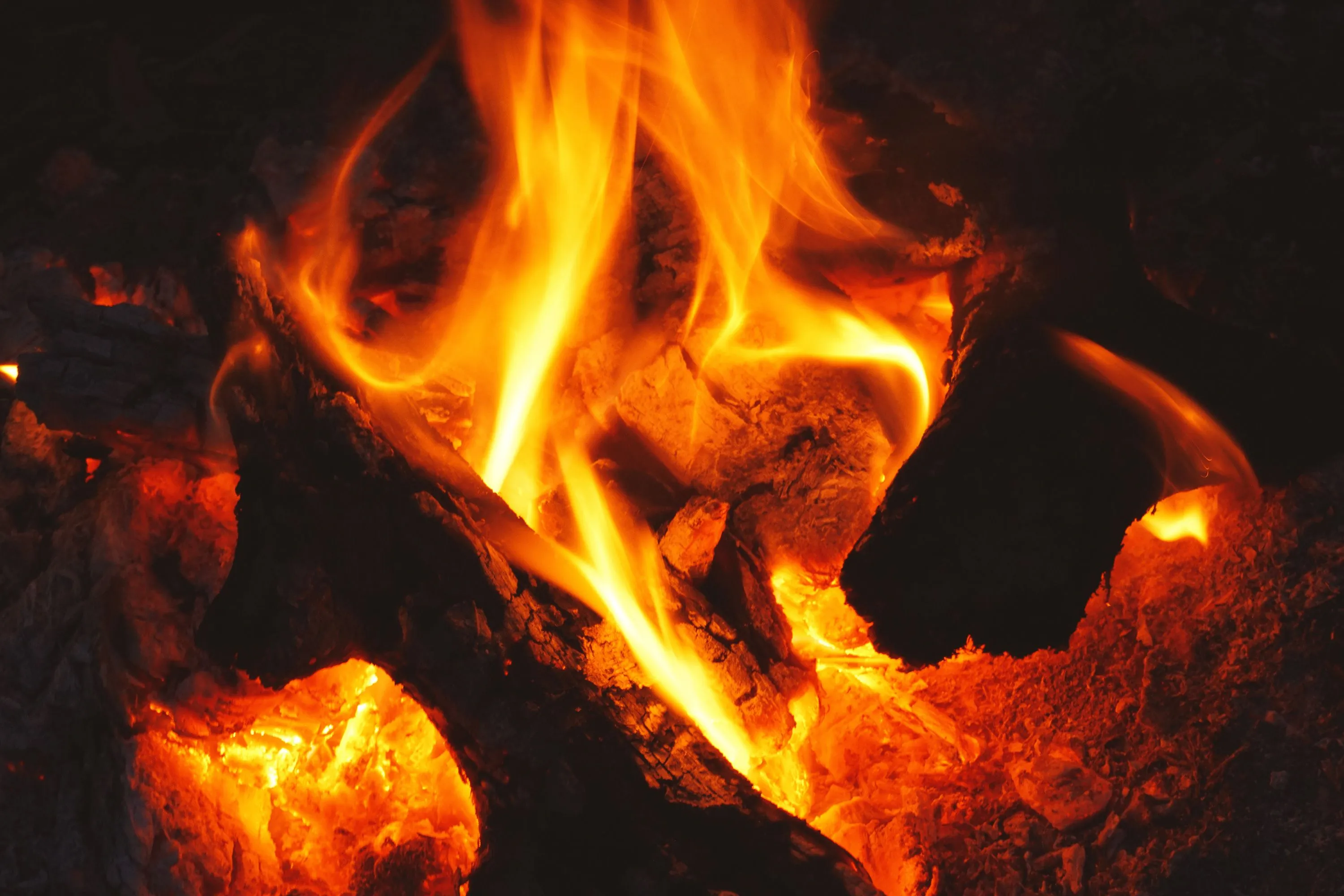 Intense close-up of flames and glowing embers in a wood fire.