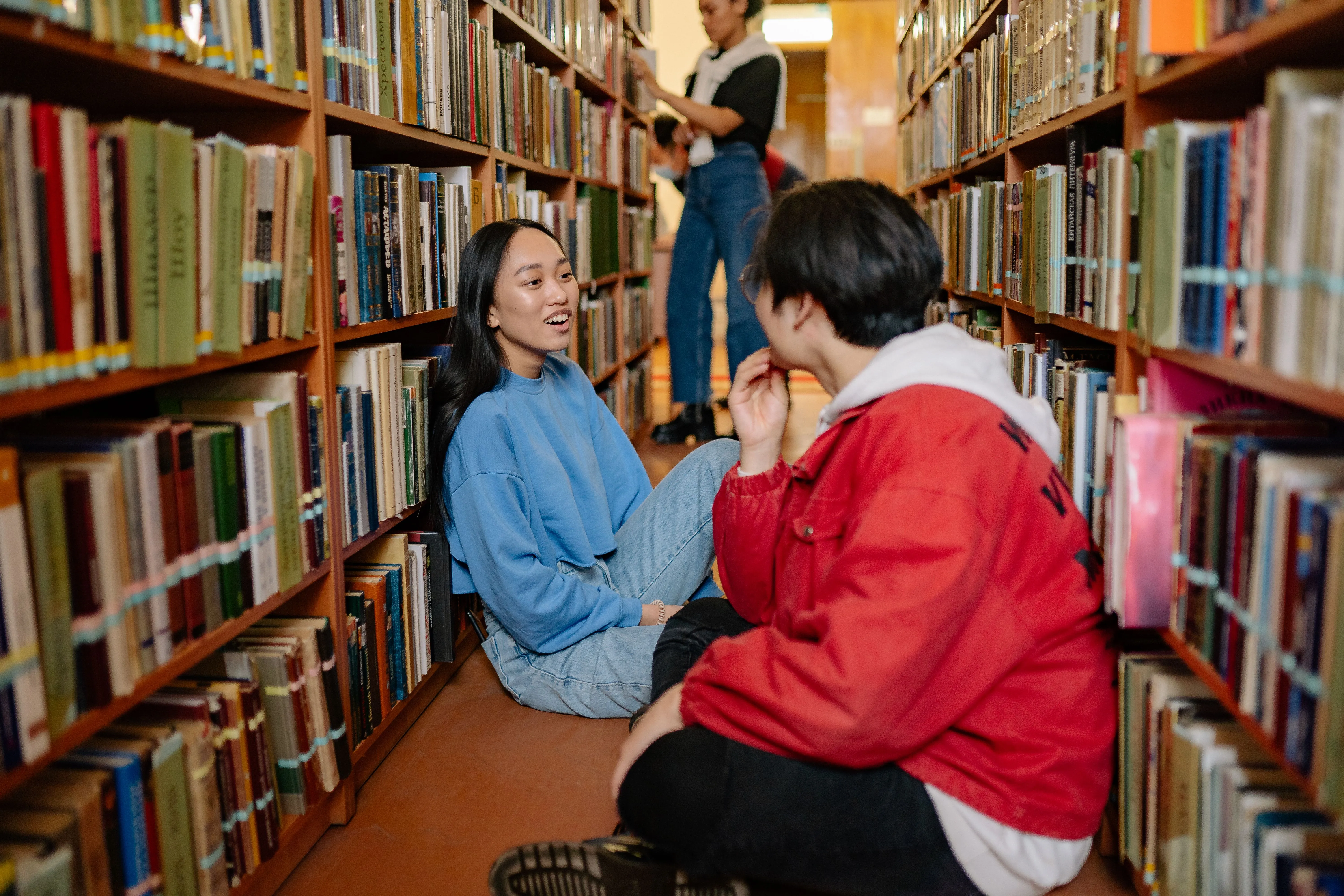 Two students having a conversation in a university library aisle.