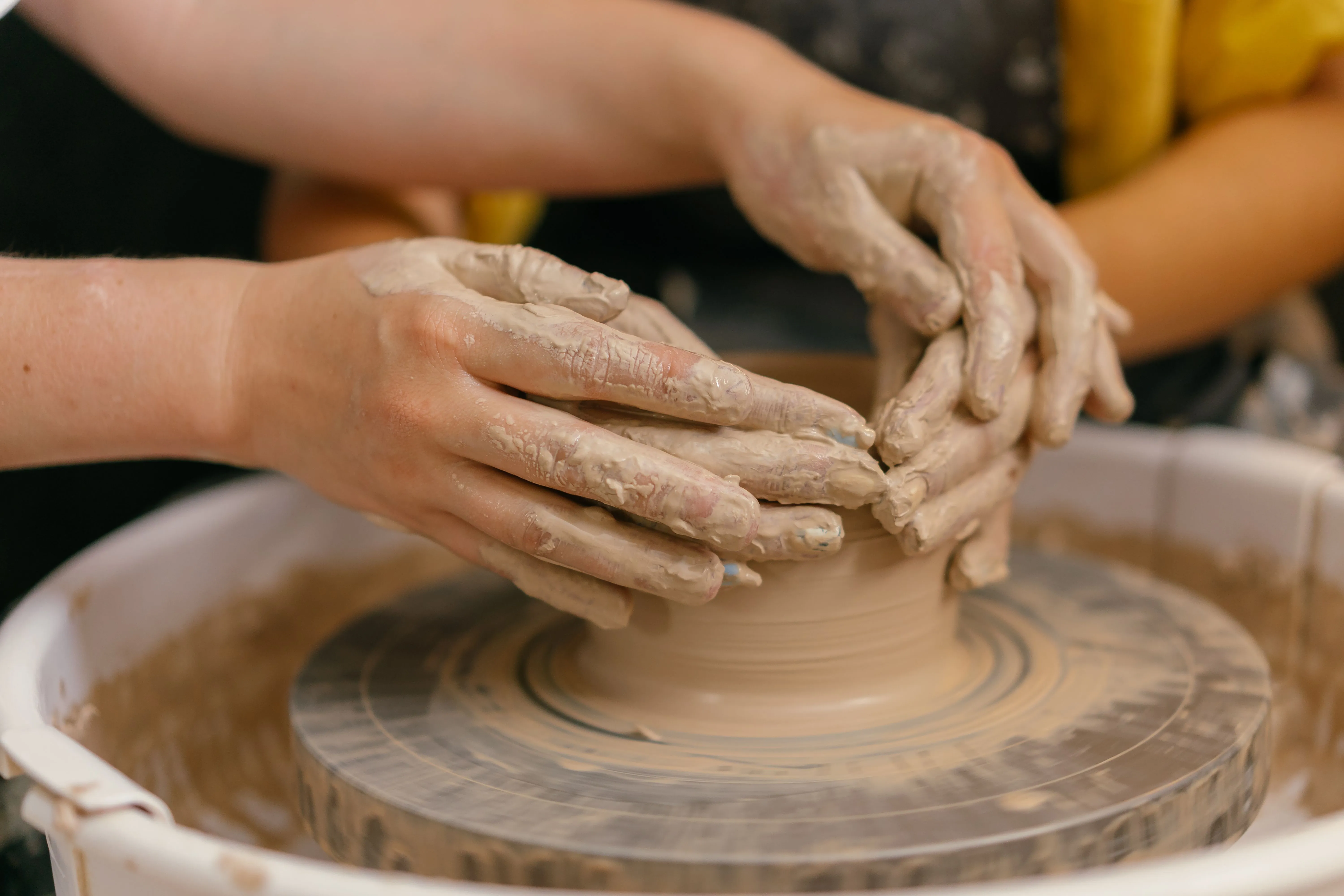 Two hands expertly mold clay on a spinning potter's wheel, highlighting artisan skill.