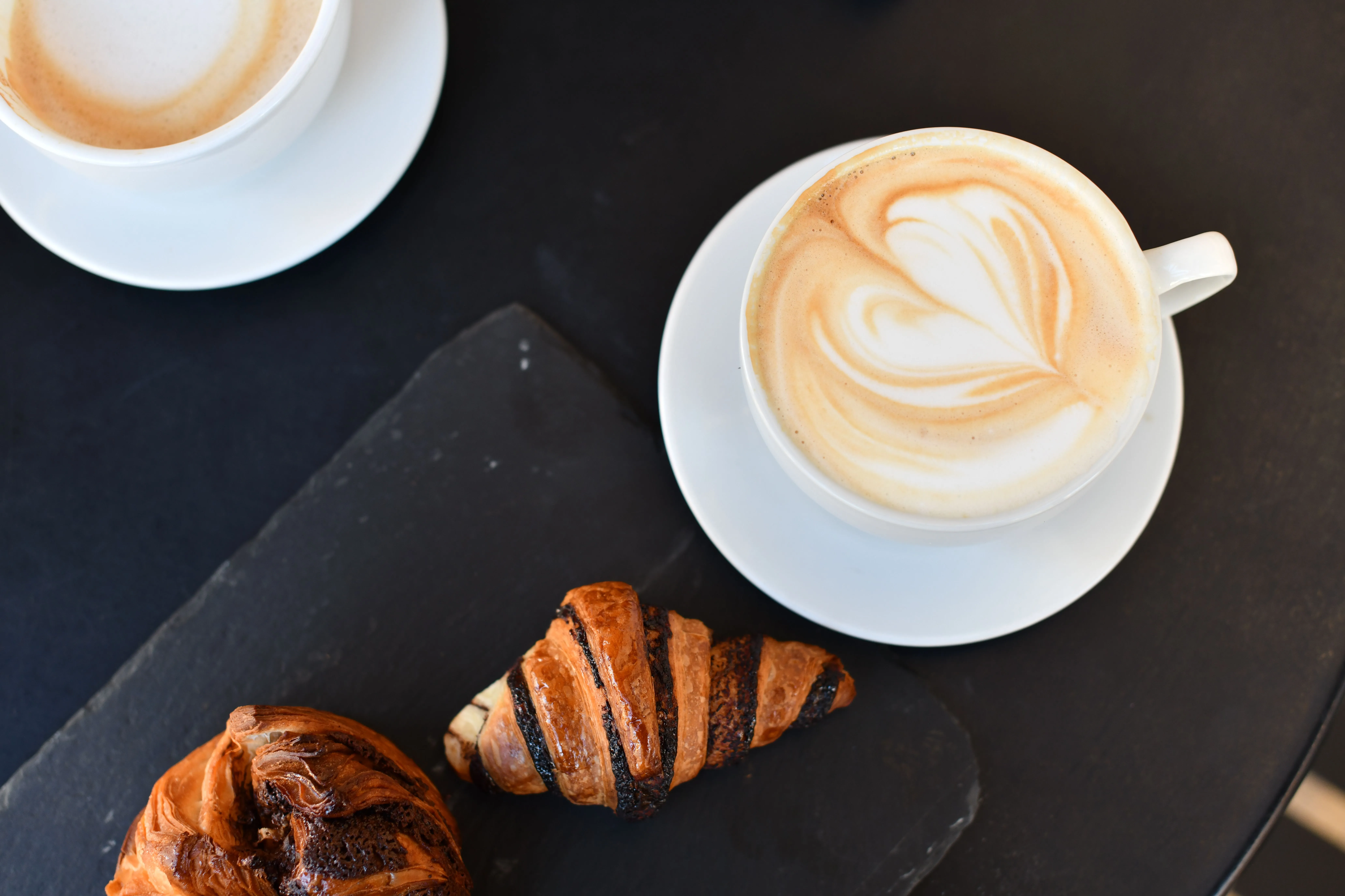 Top view of frothy cappuccino and croissants on a slate plate, perfect breakfast setup.