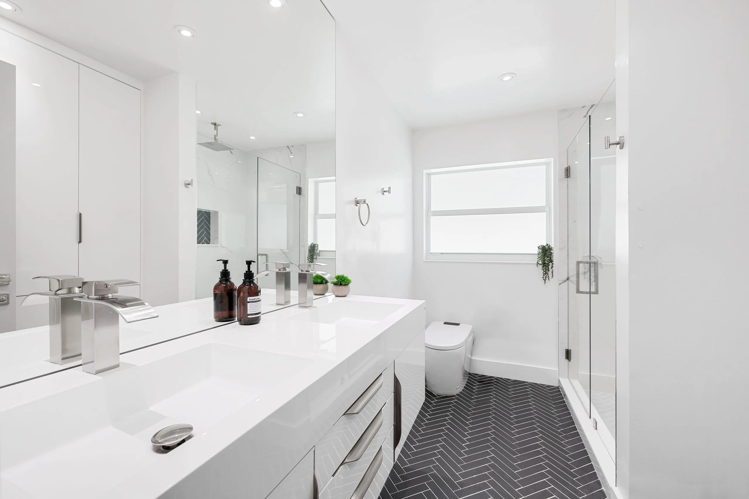 Modern white bathroom featuring sleek fixtures and herringbone flooring design.