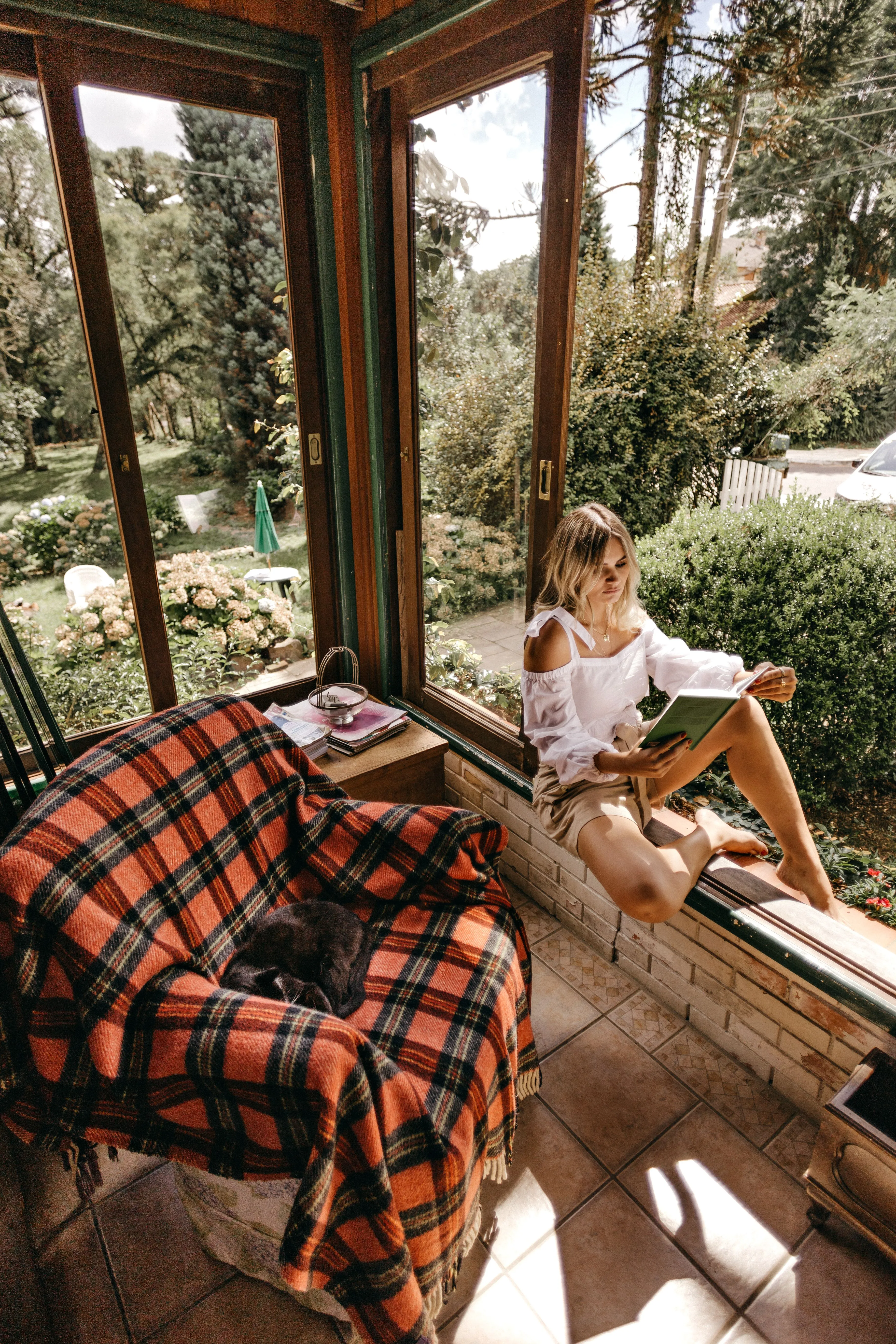 Woman enjoying a relaxing afternoon reading by a window with a garden view.