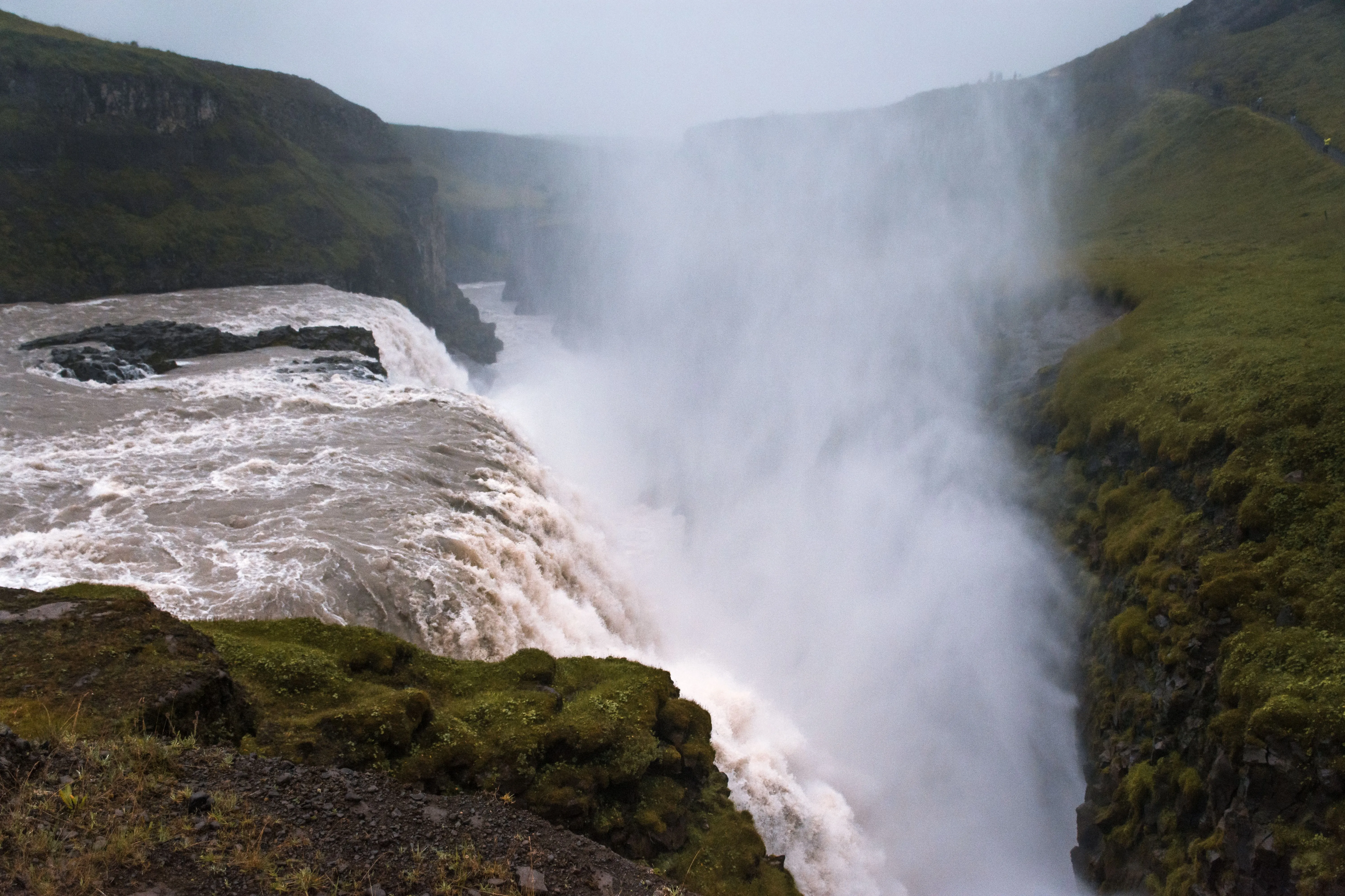 Majestic Gullfoss waterfall with mist and lush greenery in Iceland.