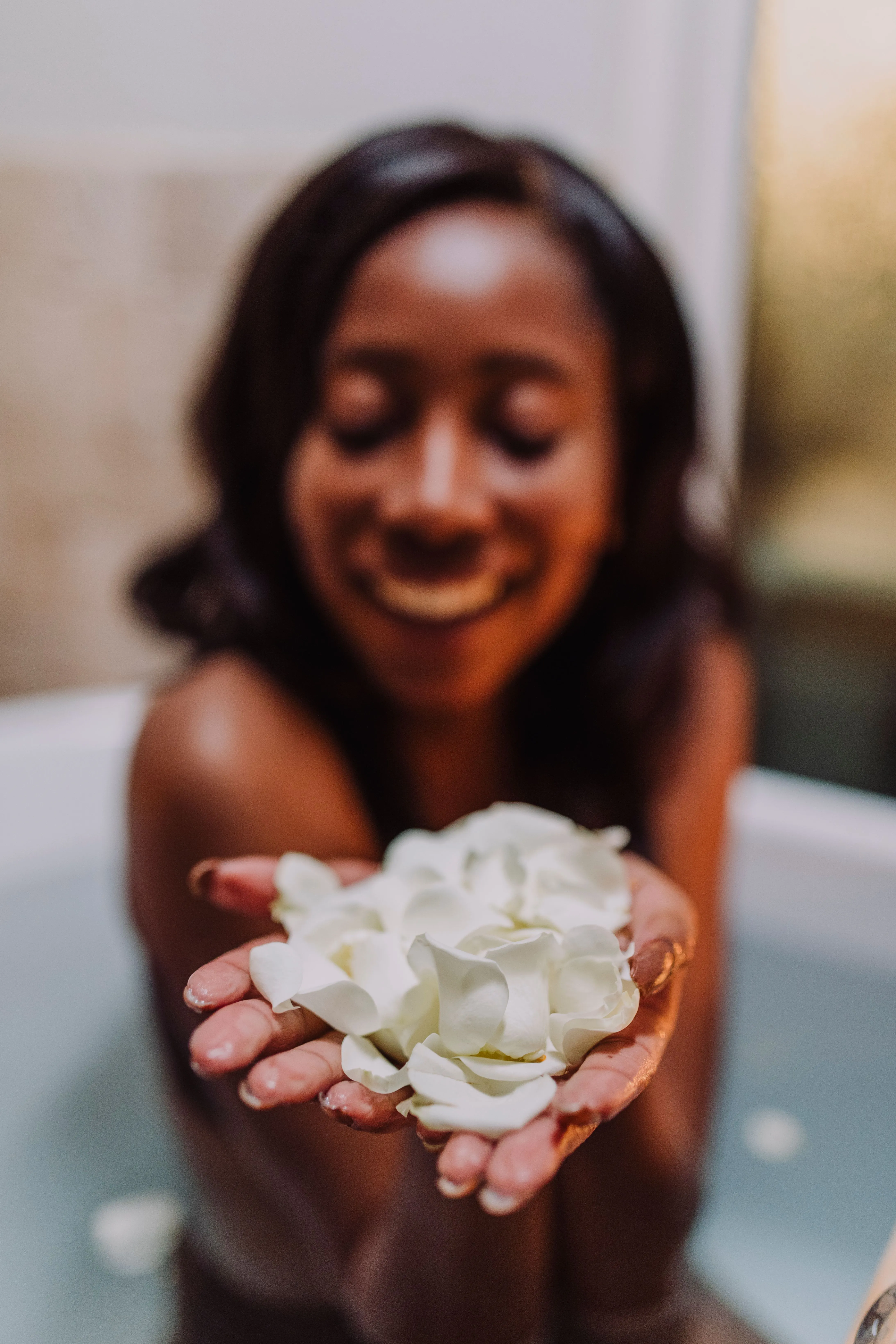 A joyful woman holding white petals while relaxing in a bath, creating a serene atmosphere.