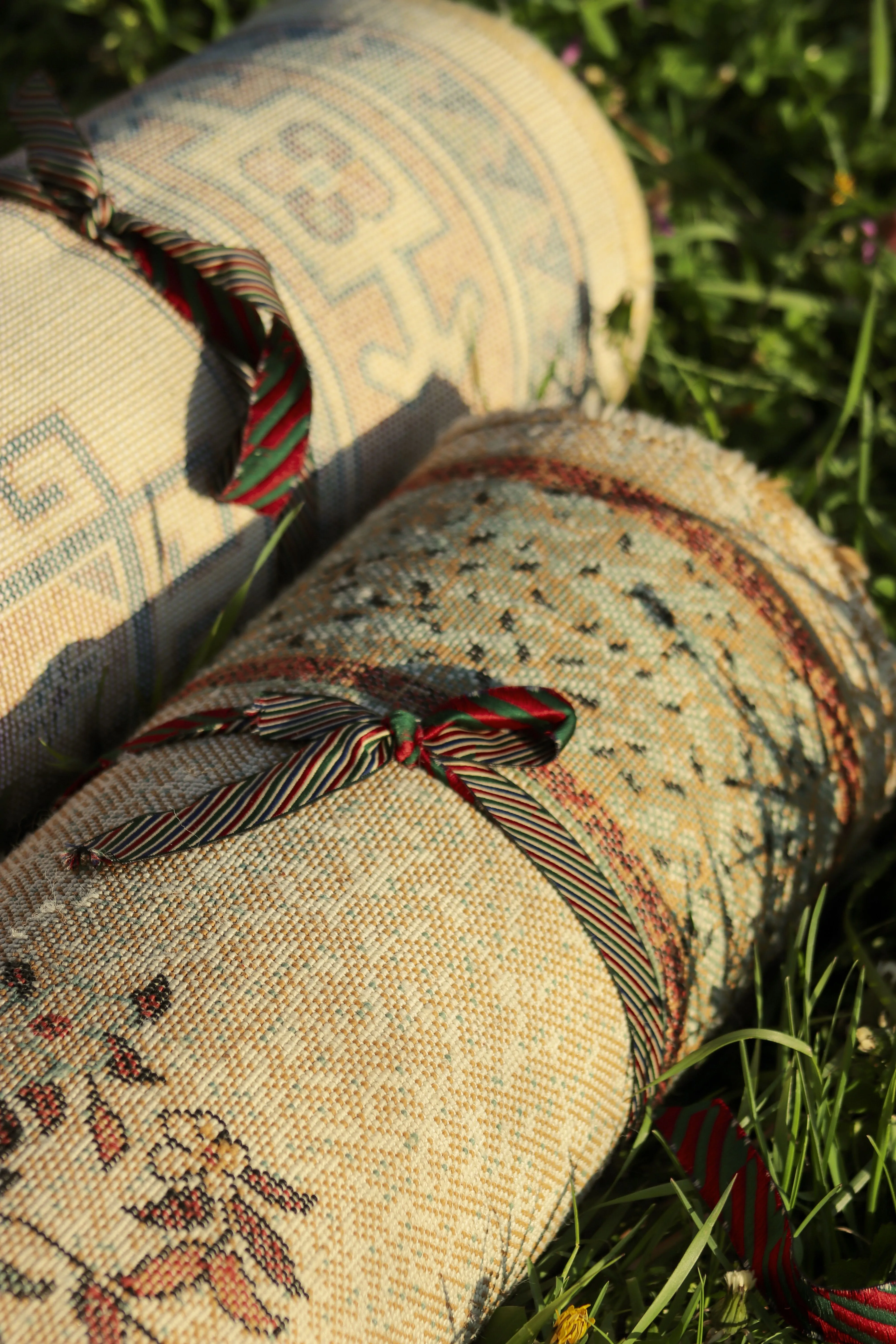 Close-up of decorative rolled-up tapestry blankets with bows on grass, highlighting intricate patterns.