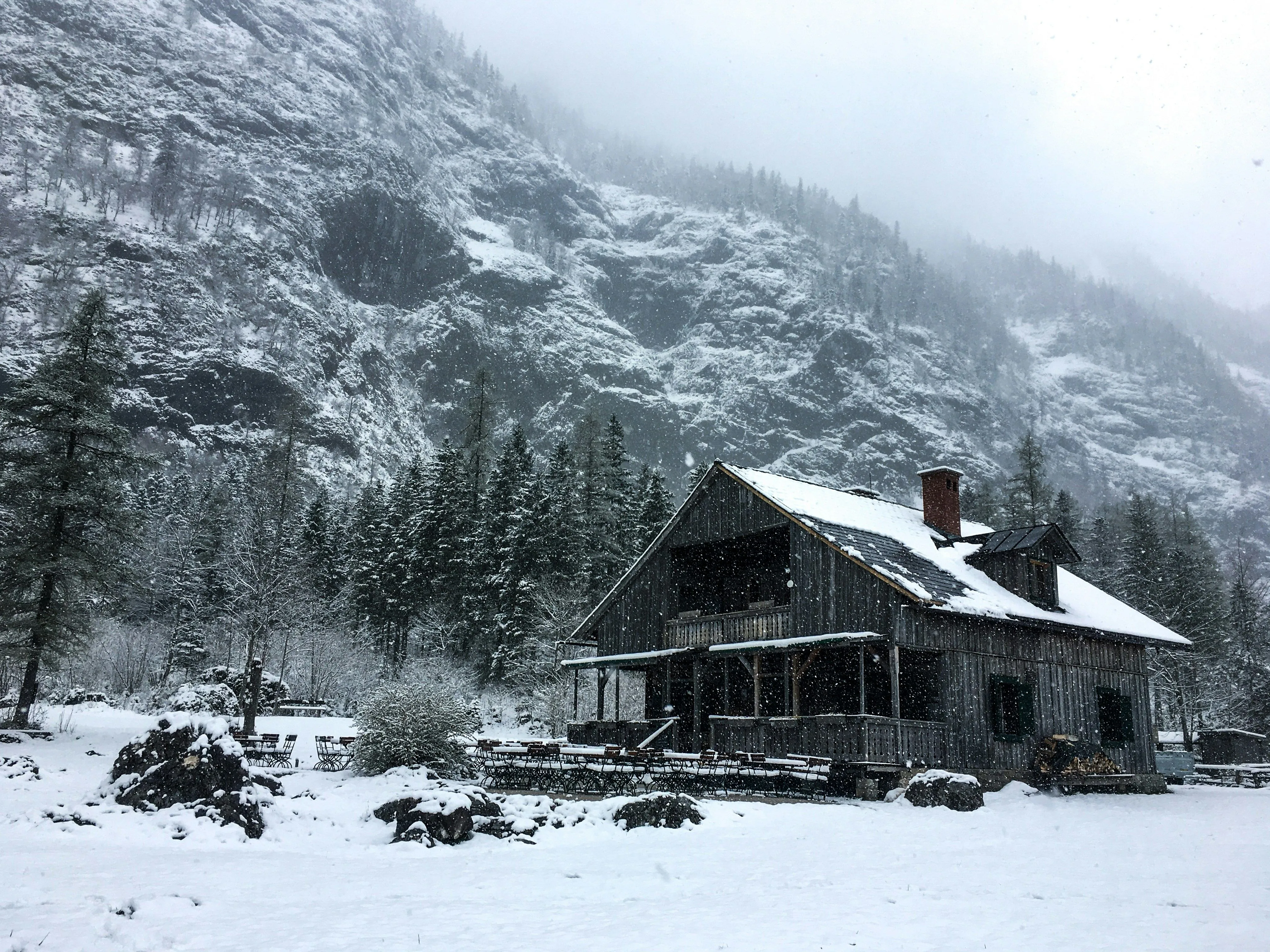 A snowy wooden cabin nestled in a winter mountain landscape with trees and fog.