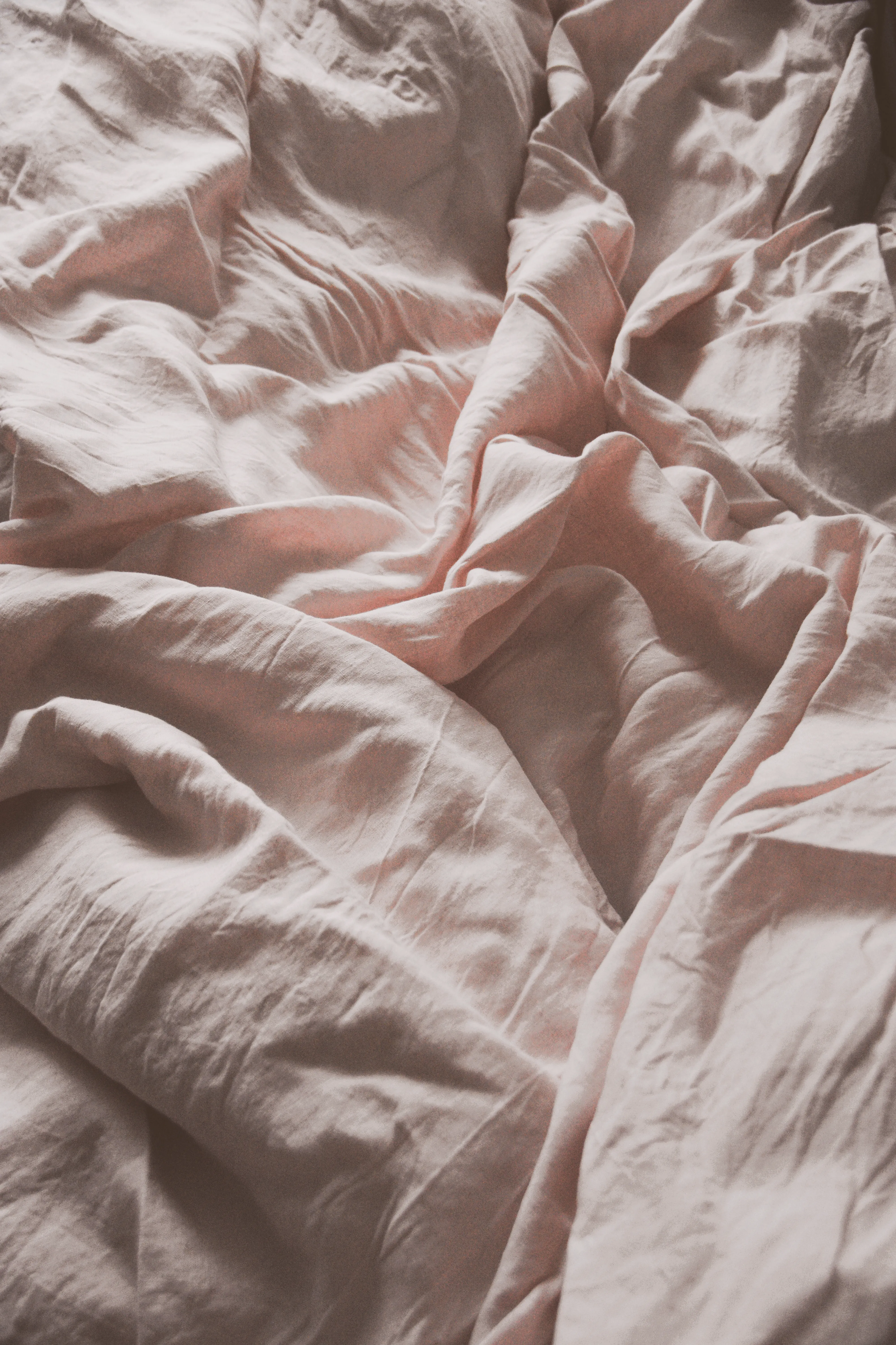 A close-up of crinkled pink bed sheets highlighting soft fabric texture.