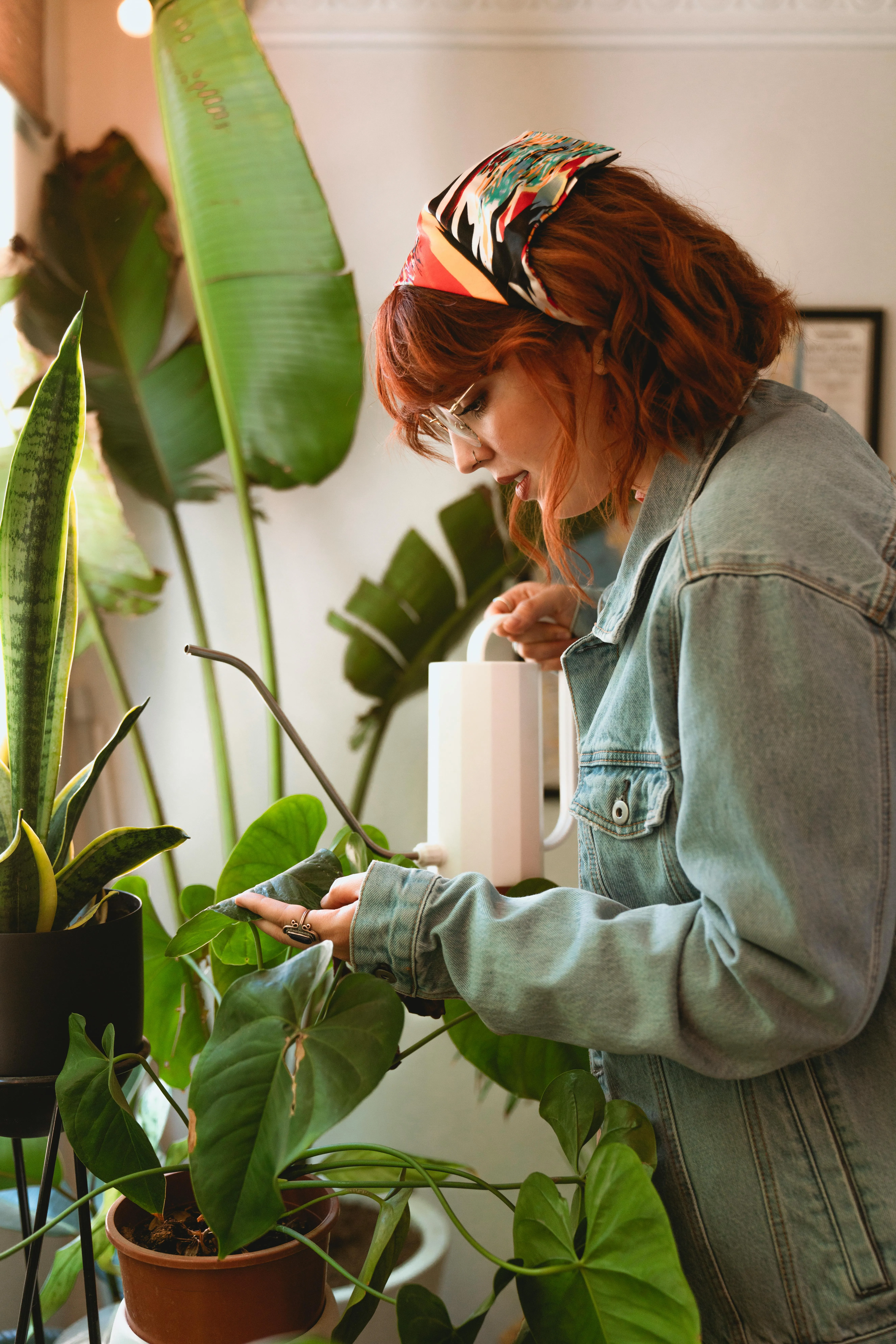 Young woman with red hair watering houseplants indoors, nurturing greenery.