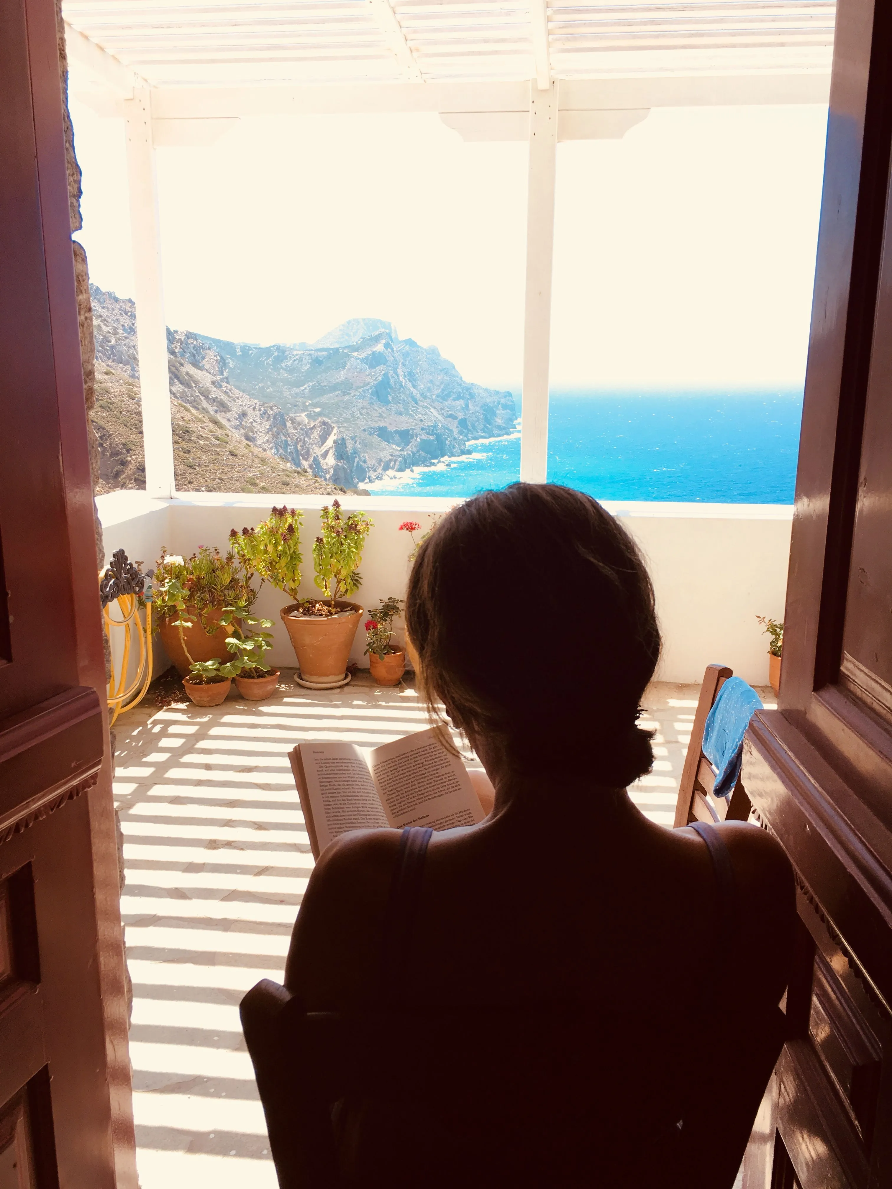 Woman reading on a Greek balcony with stunning sea and mountain view.