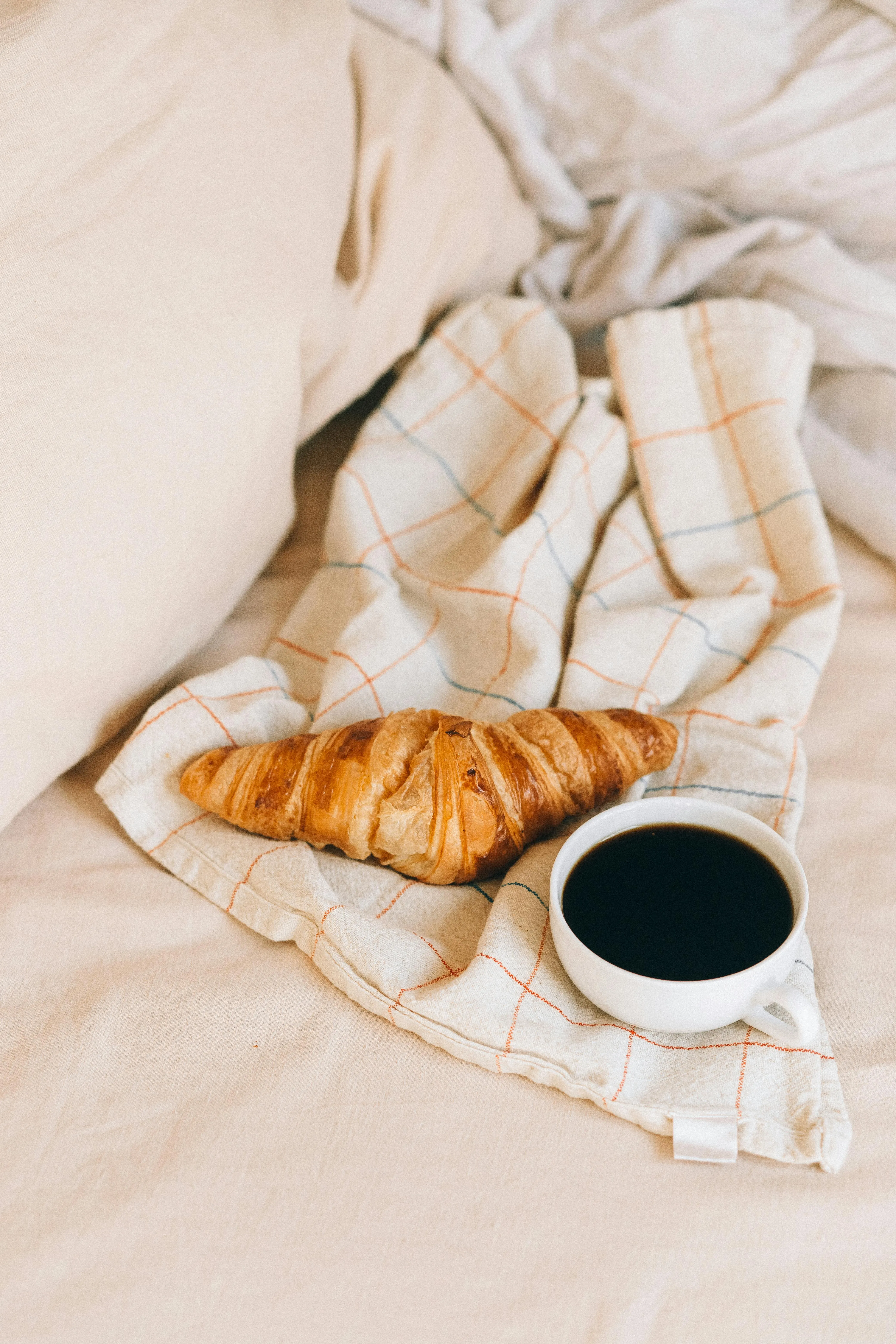 Warm morning scene with coffee and croissant on a kitchen towel, perfect for breakfast in bed.