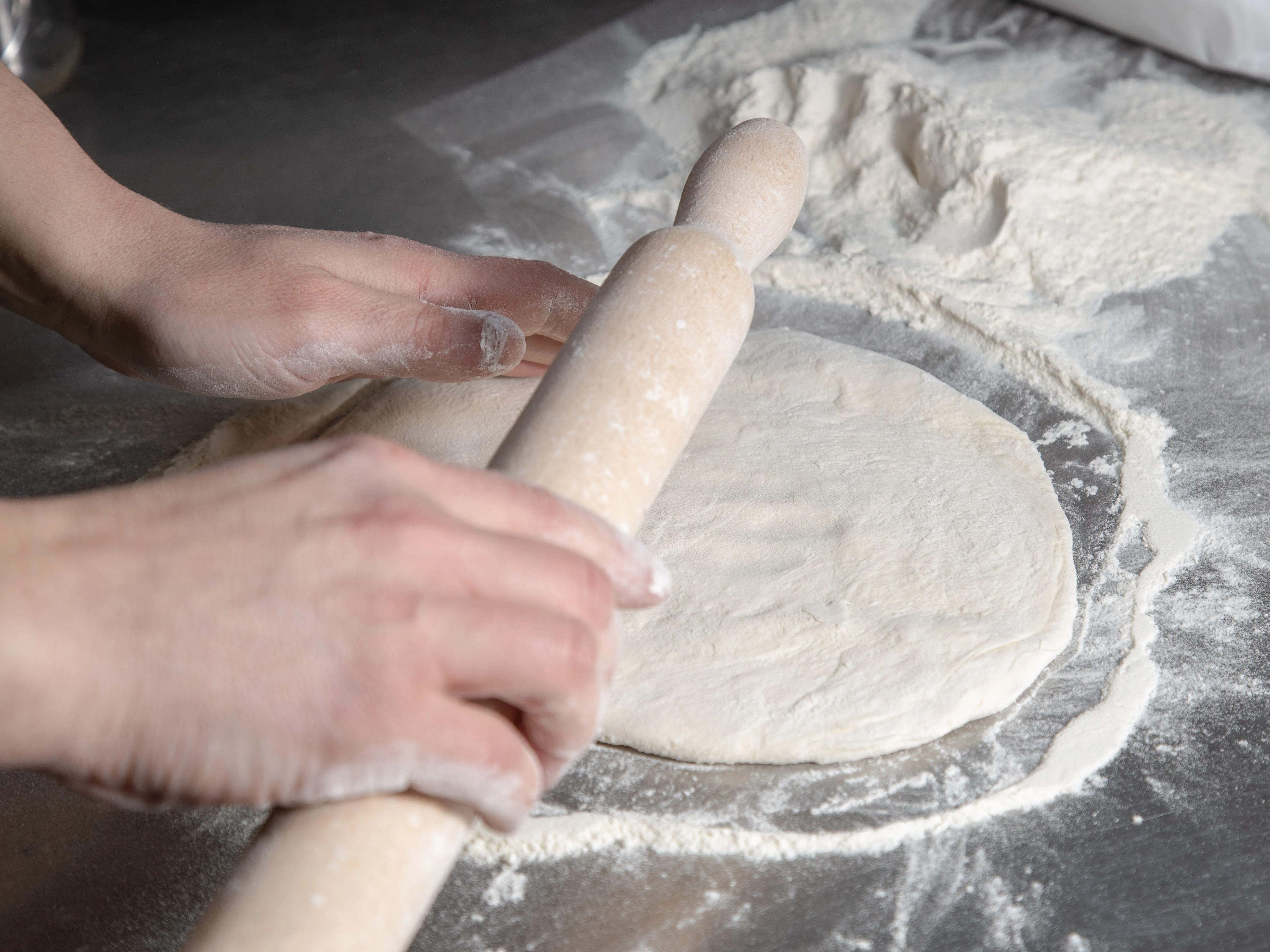Close-up of hands rolling dough on floured surface, preparing for baking.