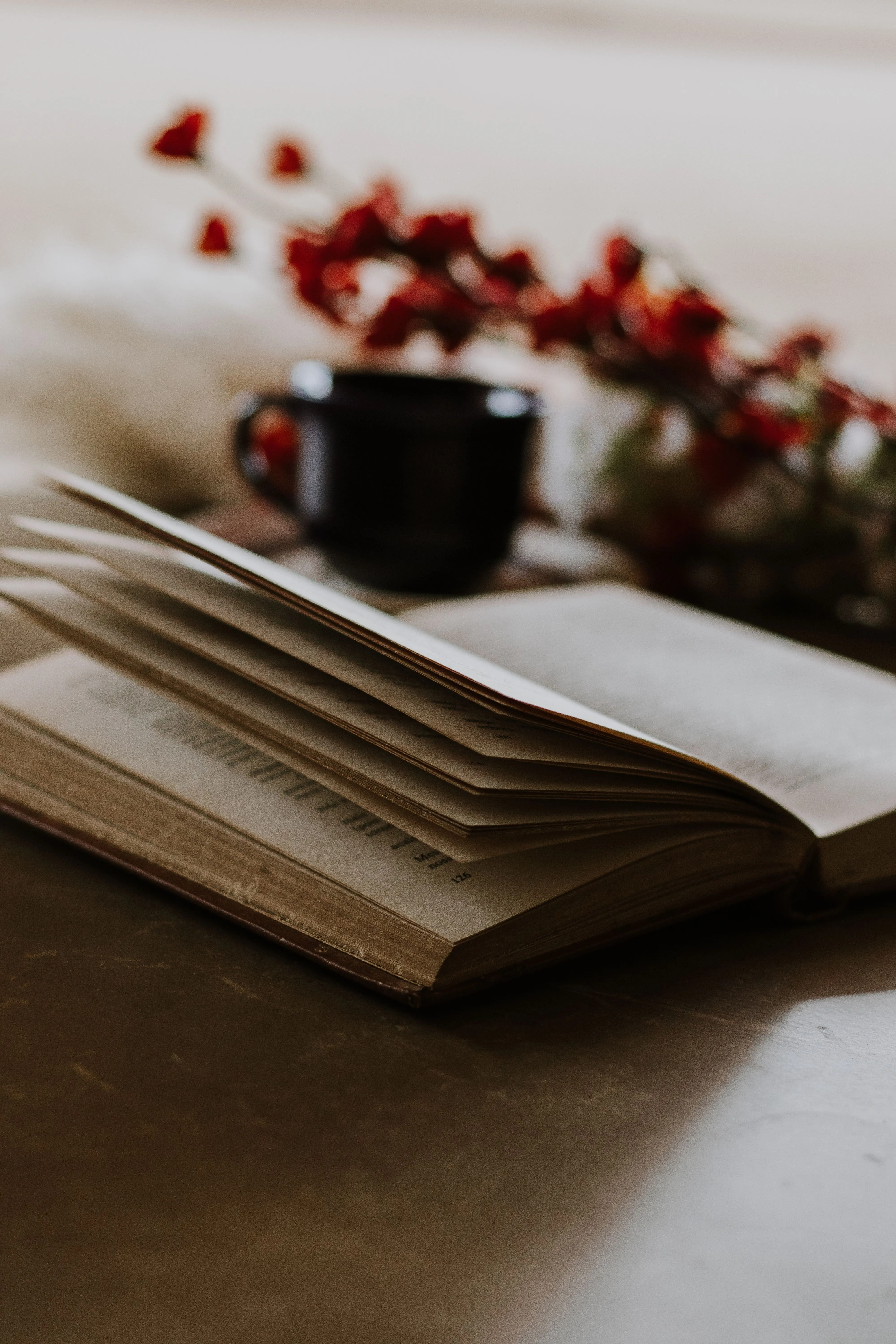 A warm and inviting setting featuring an open book, cup of coffee, and red flowers on a table.