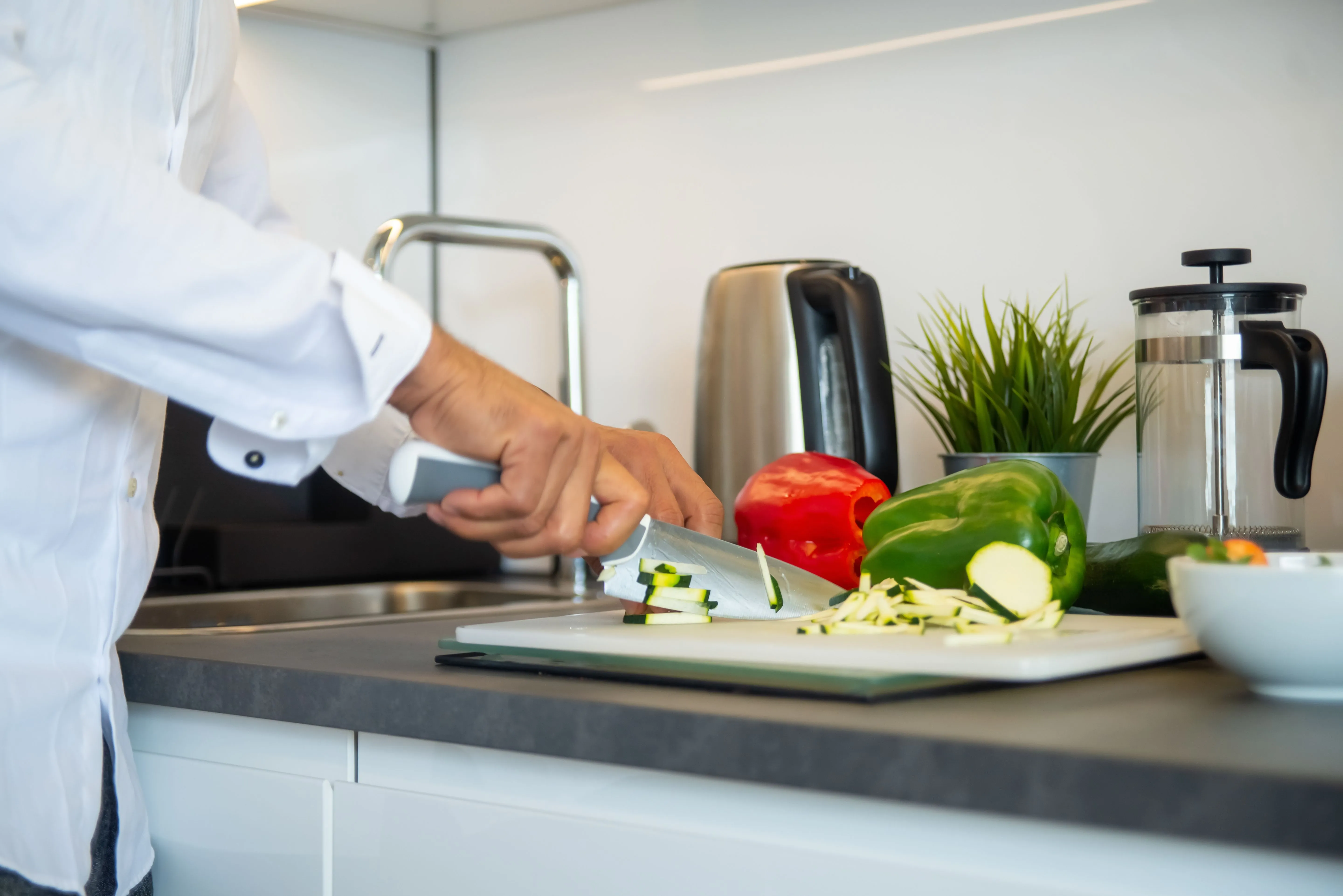 Man slicing bell peppers in a contemporary kitchen with a kettle.