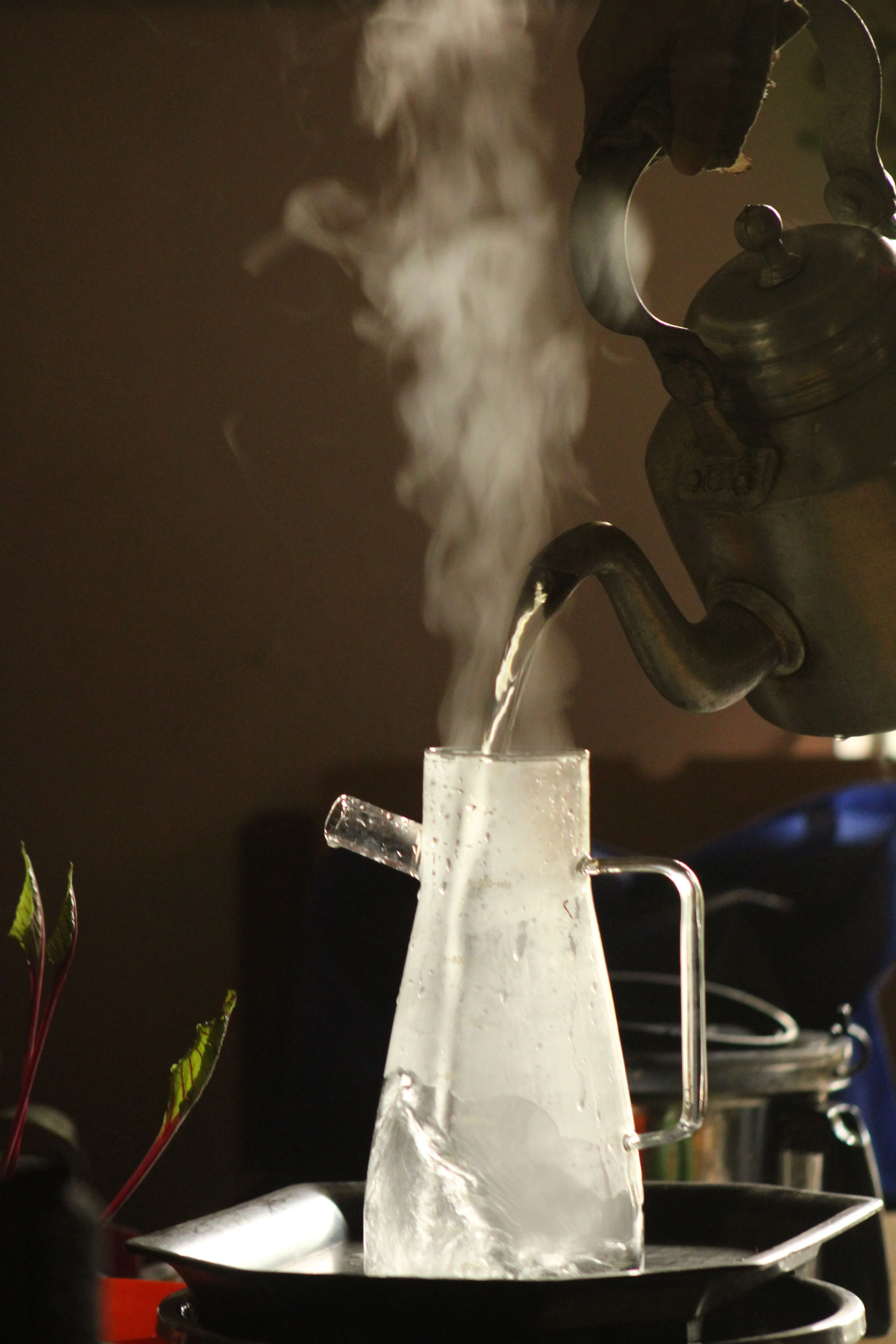 Steam rising as hot water is poured into a glass jug from a kettle, creating a warm ambiance.