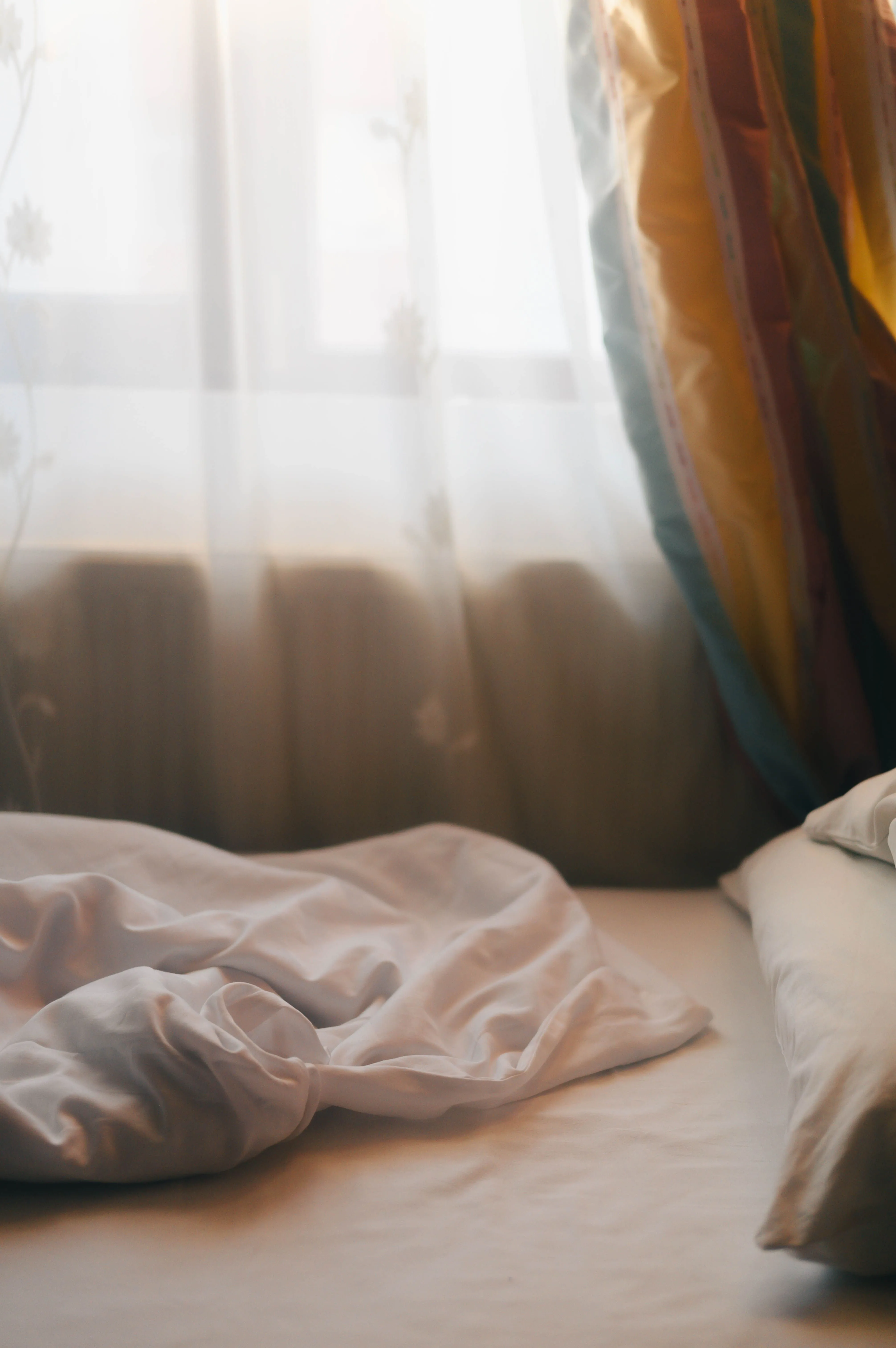 Soft morning light filters through curtains onto a neatly made bed, creating a serene ambiance.