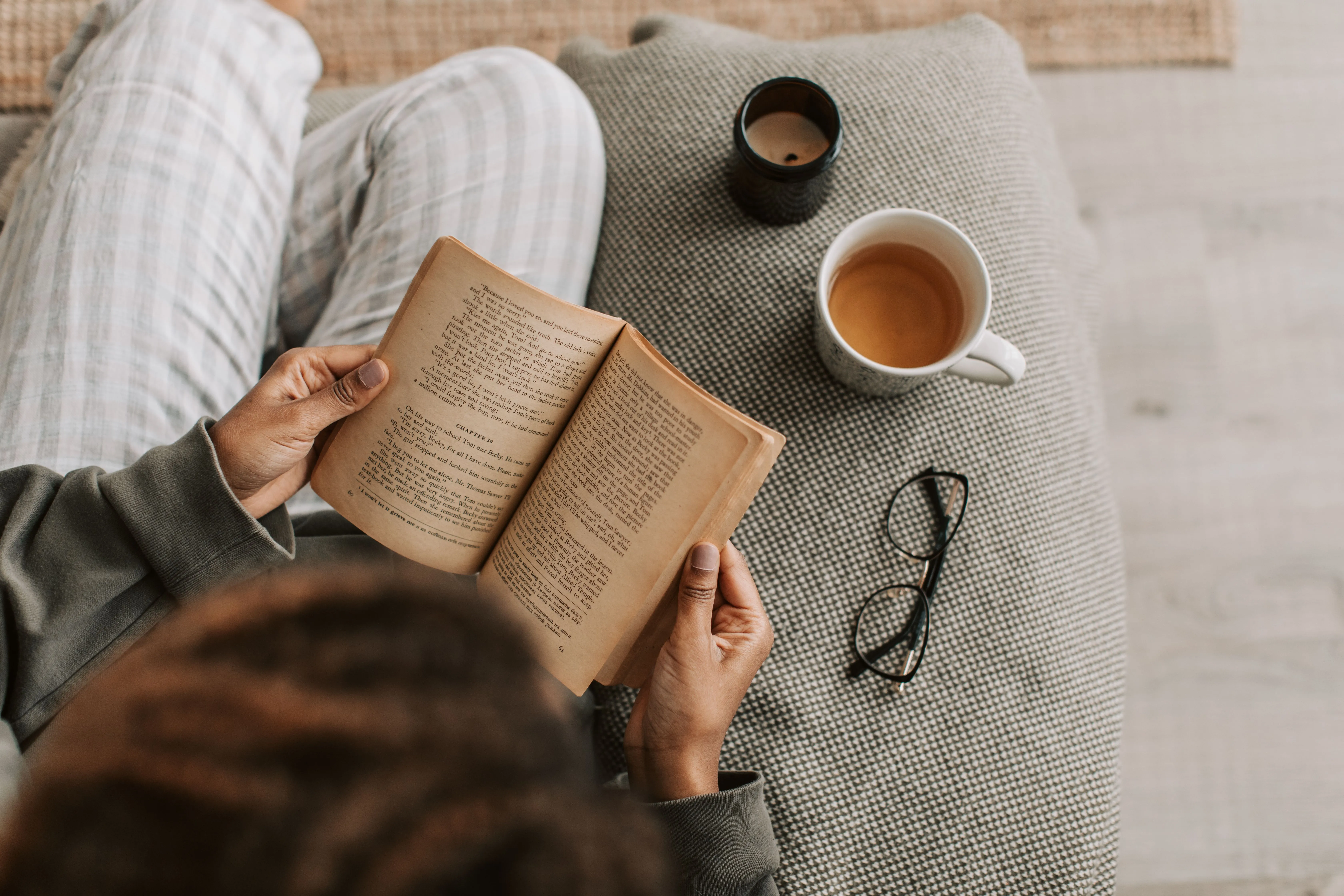 Person enjoying a relaxing time reading a book with tea indoors, perfect for leisure and comfort.