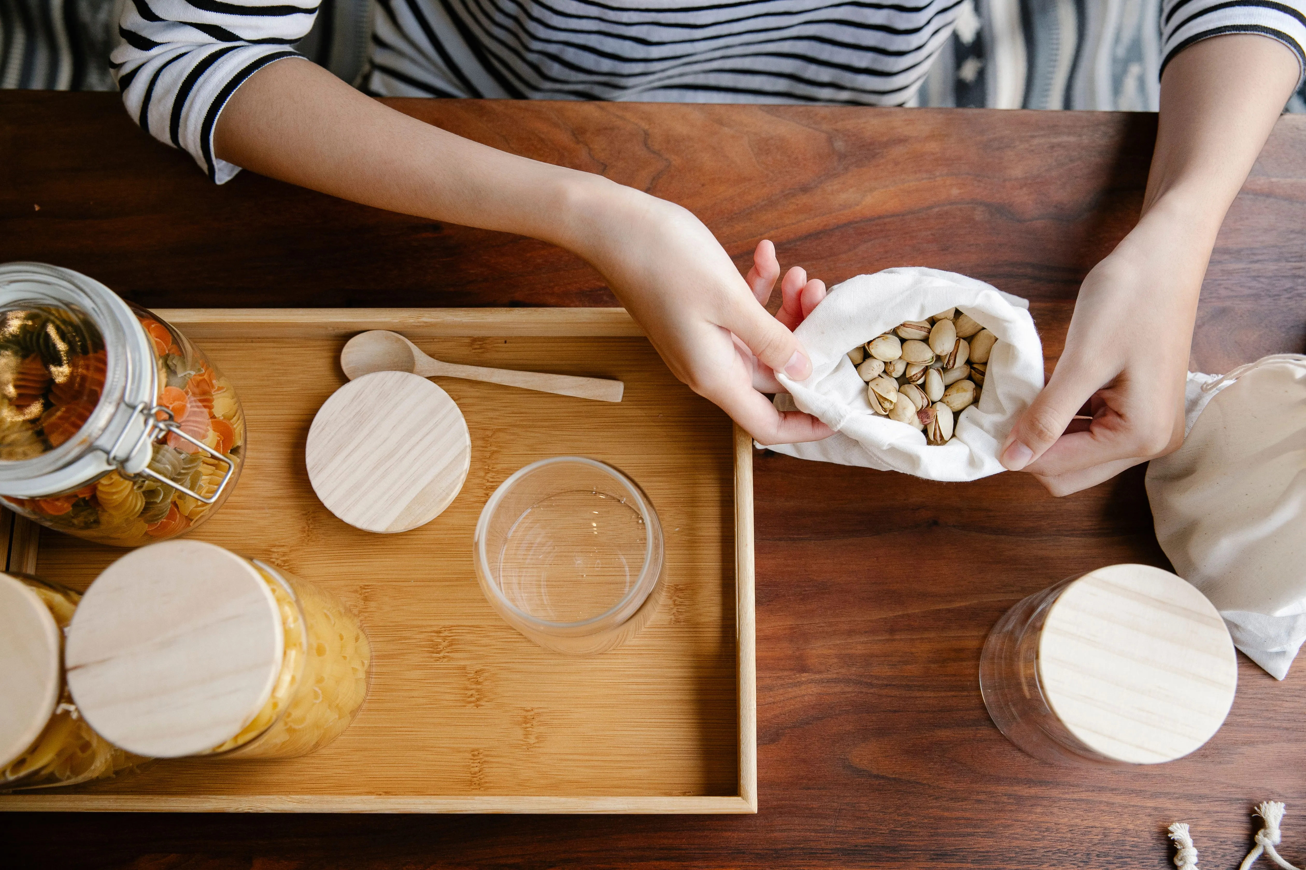 Top view of crop anonymous person holding edges of white recycling bag with pistachios on wooden table