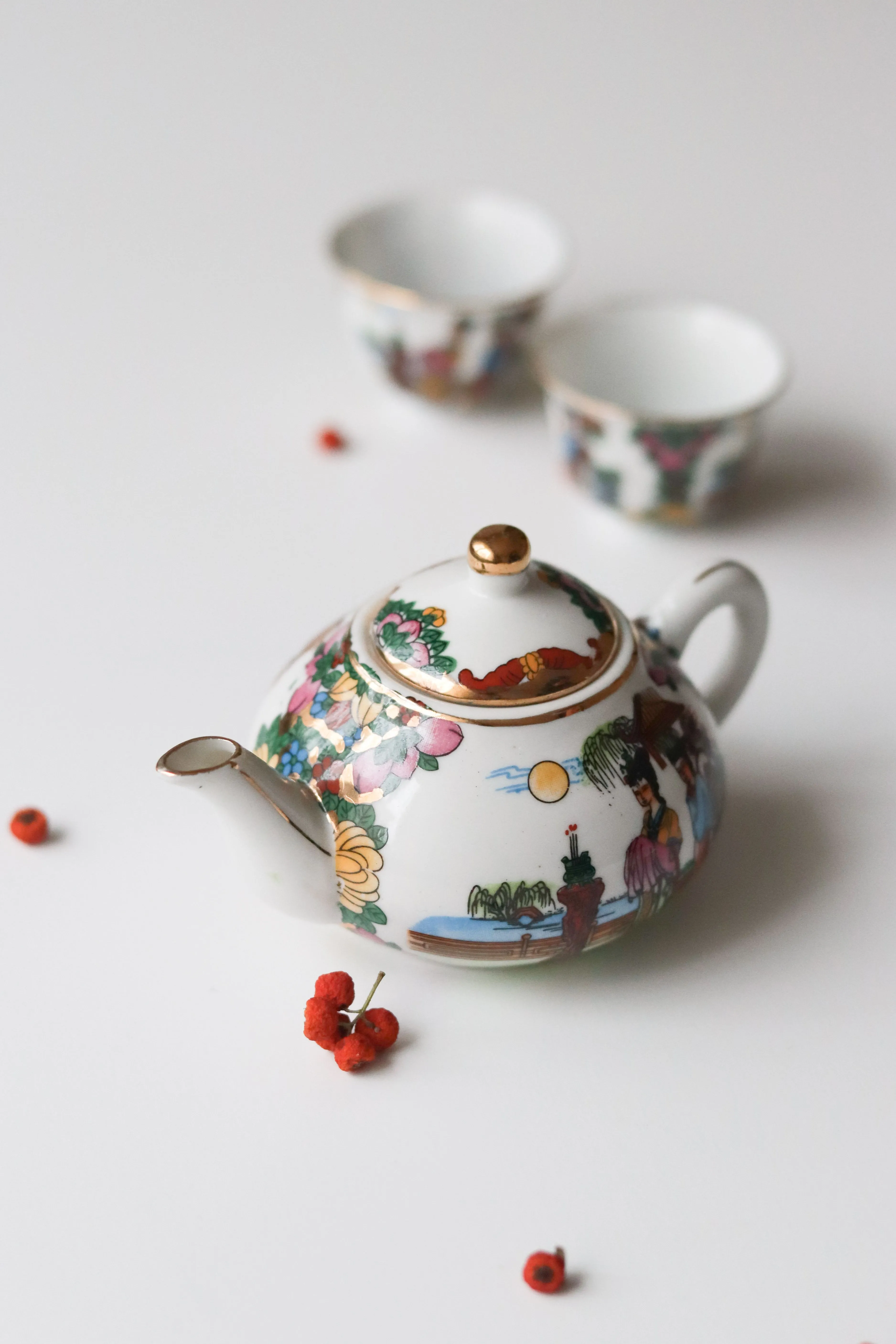 Decorative porcelain teapot with matching cups on a white background featuring artful design.