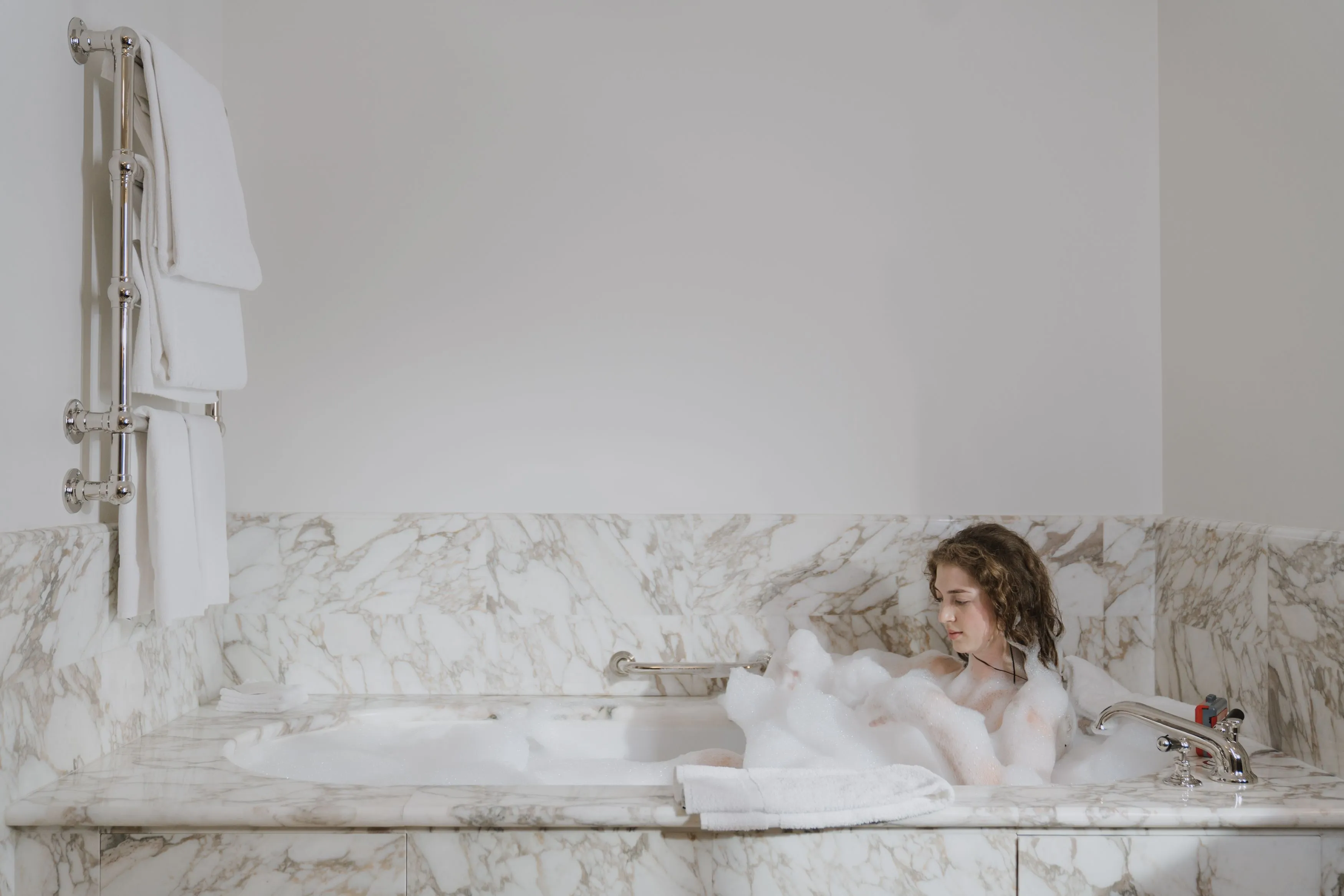 A woman enjoys a calming bubble bath in a luxurious marble bathroom.