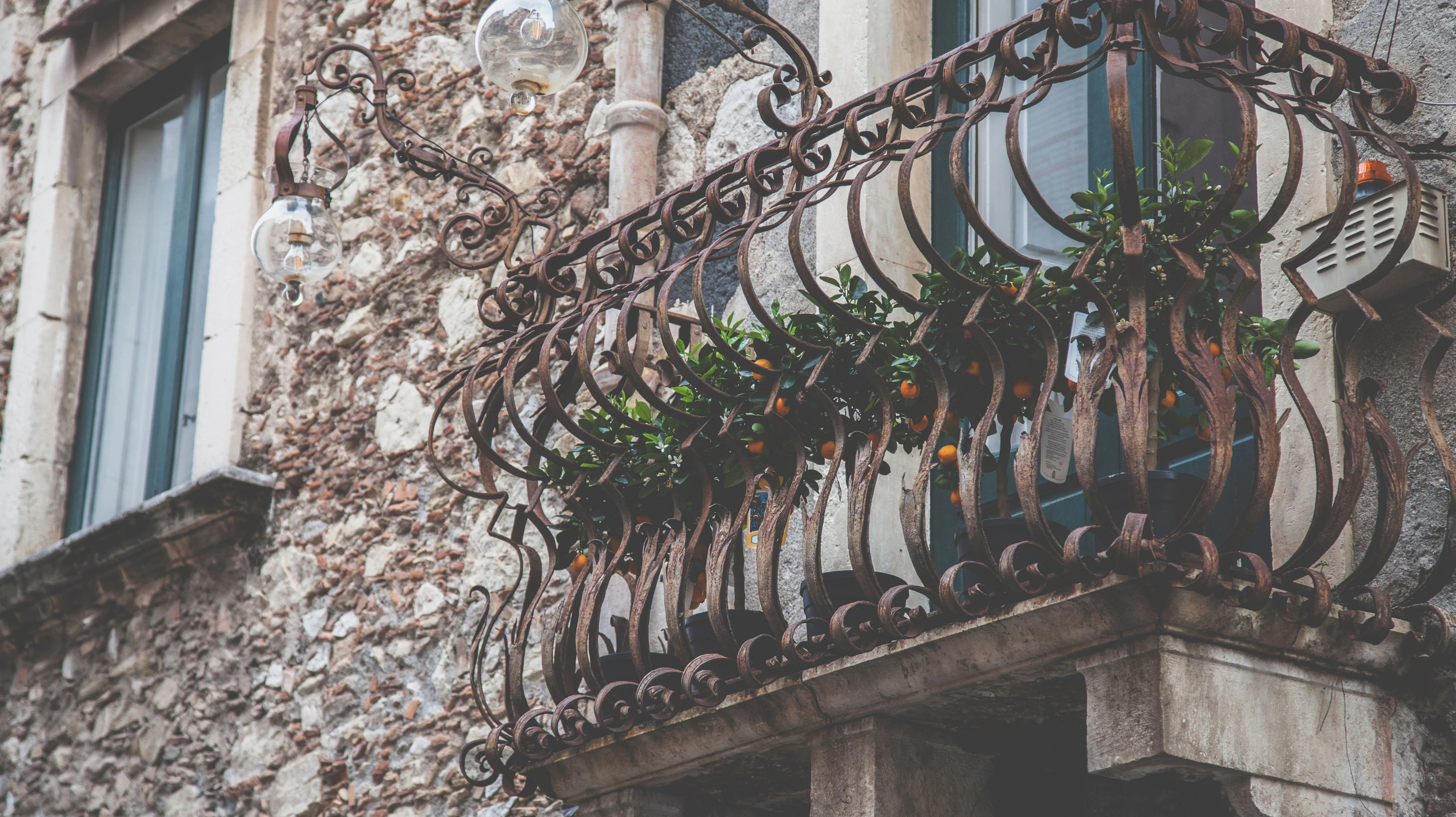 A charming rustic balcony with detailed iron railing and fresh green potted plants.