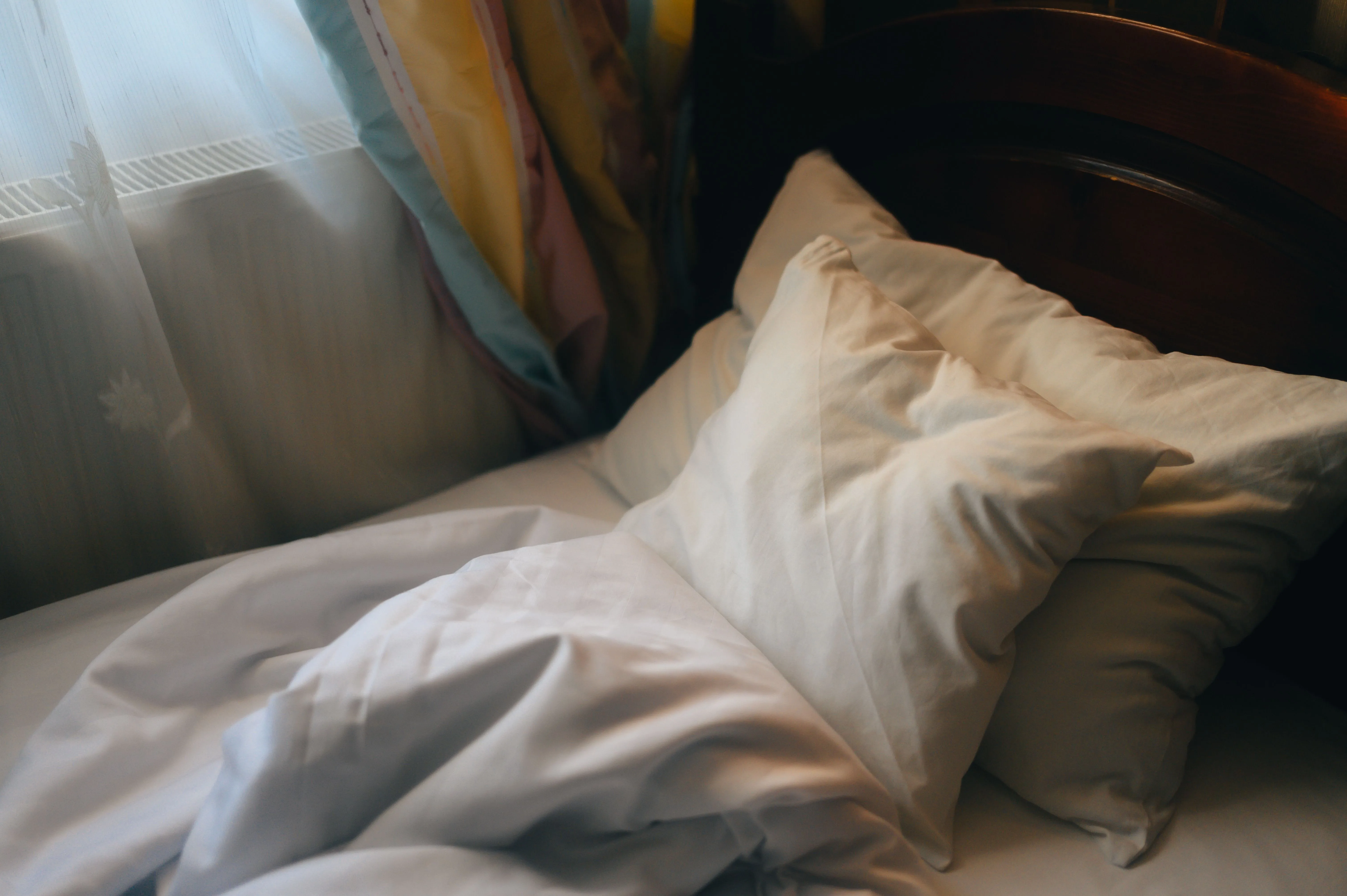 Inviting unmade bed with soft pillows in morning light, creating a cozy atmosphere.