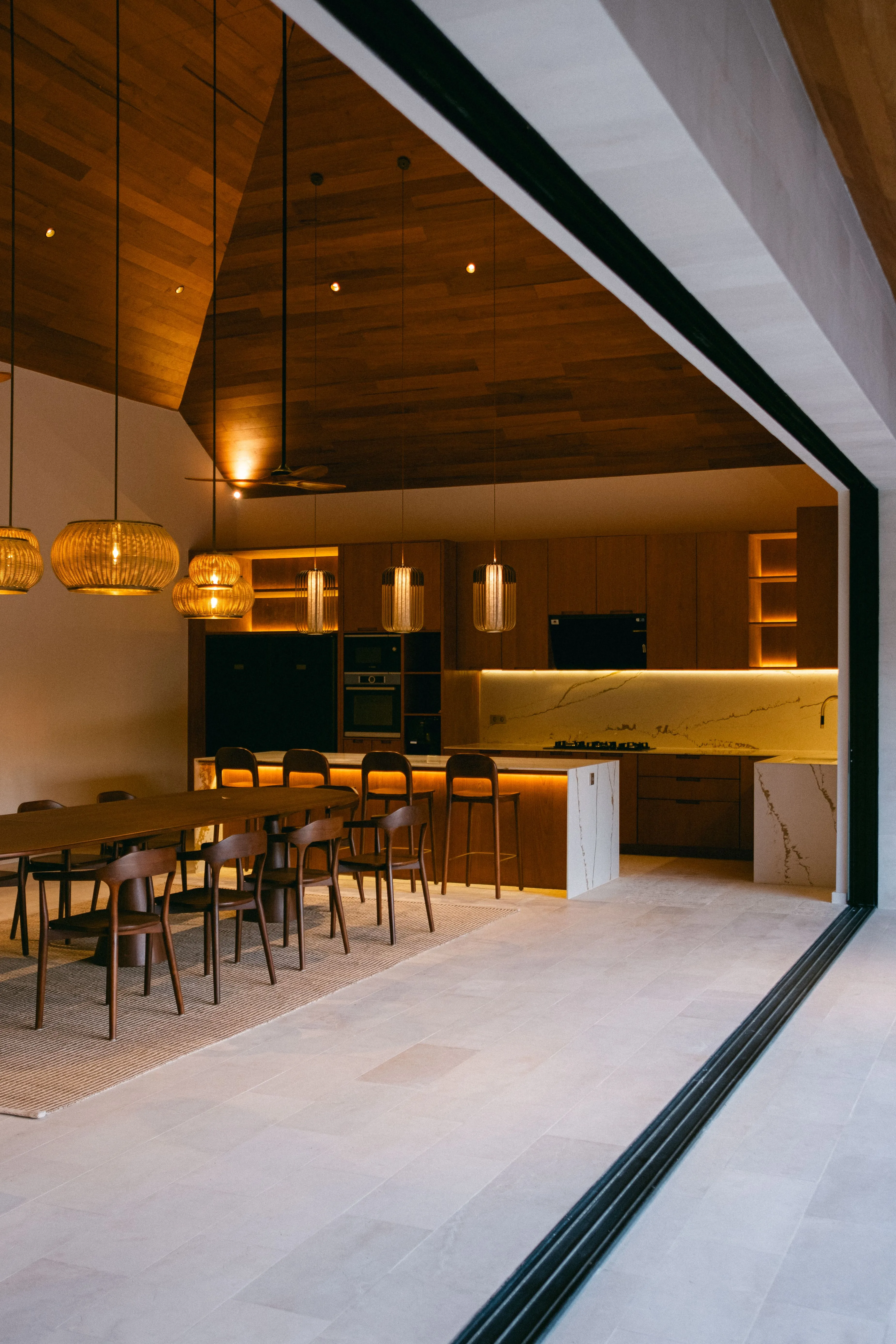 Spacious modern kitchen and dining room with wooden decor, pendant lights, and sleek furniture.
