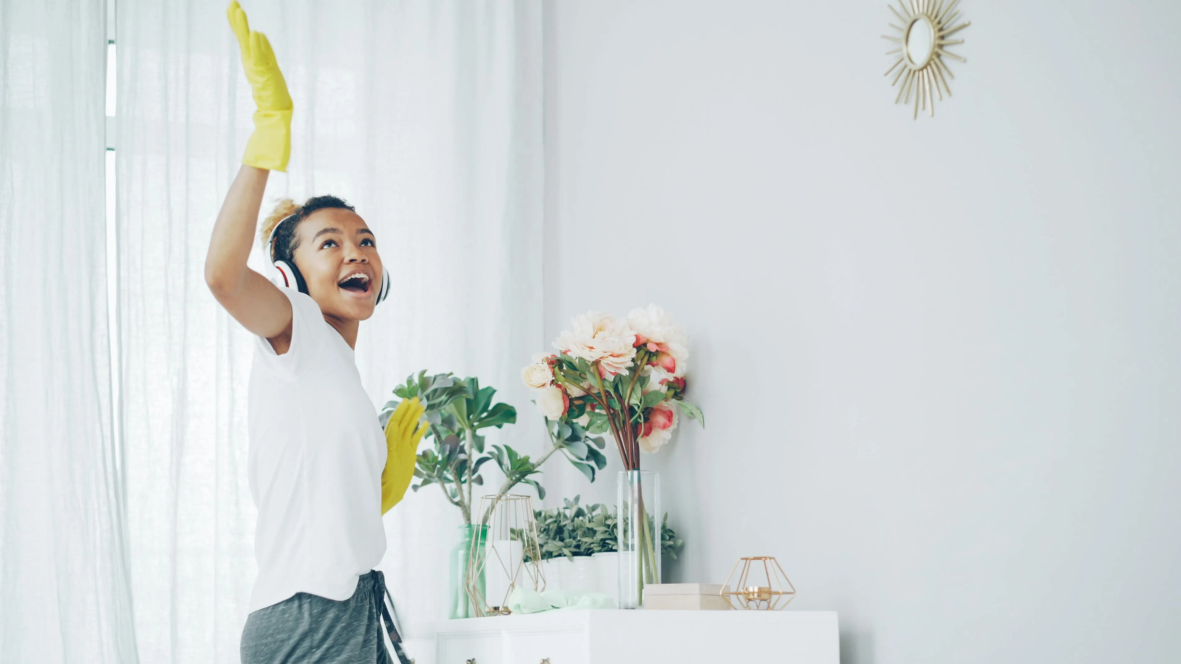 Happy woman with headphones dances while cleaning a bright, stylish room.