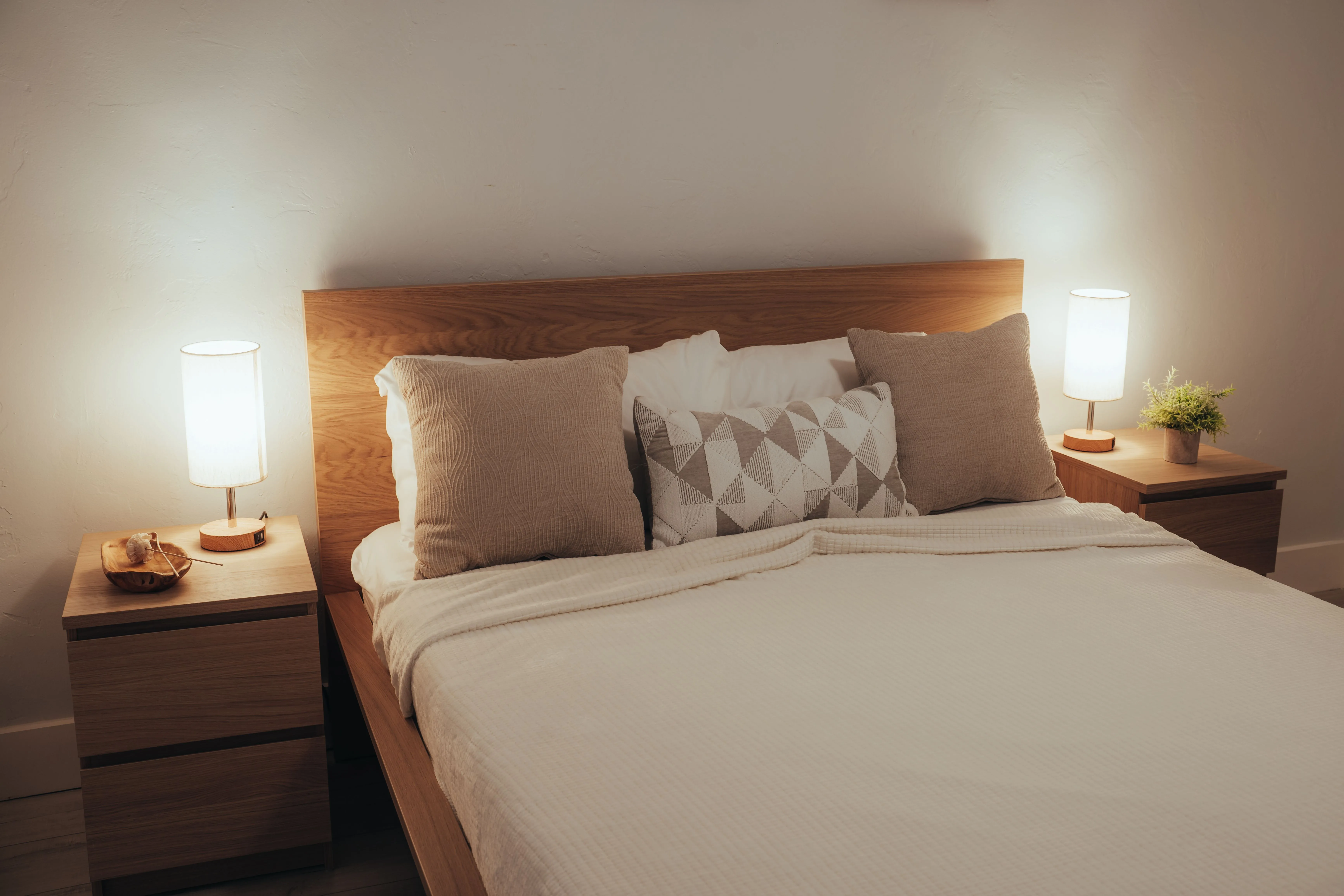 A minimalist bedroom featuring soft lighting, modern furniture, and cozy bedding.